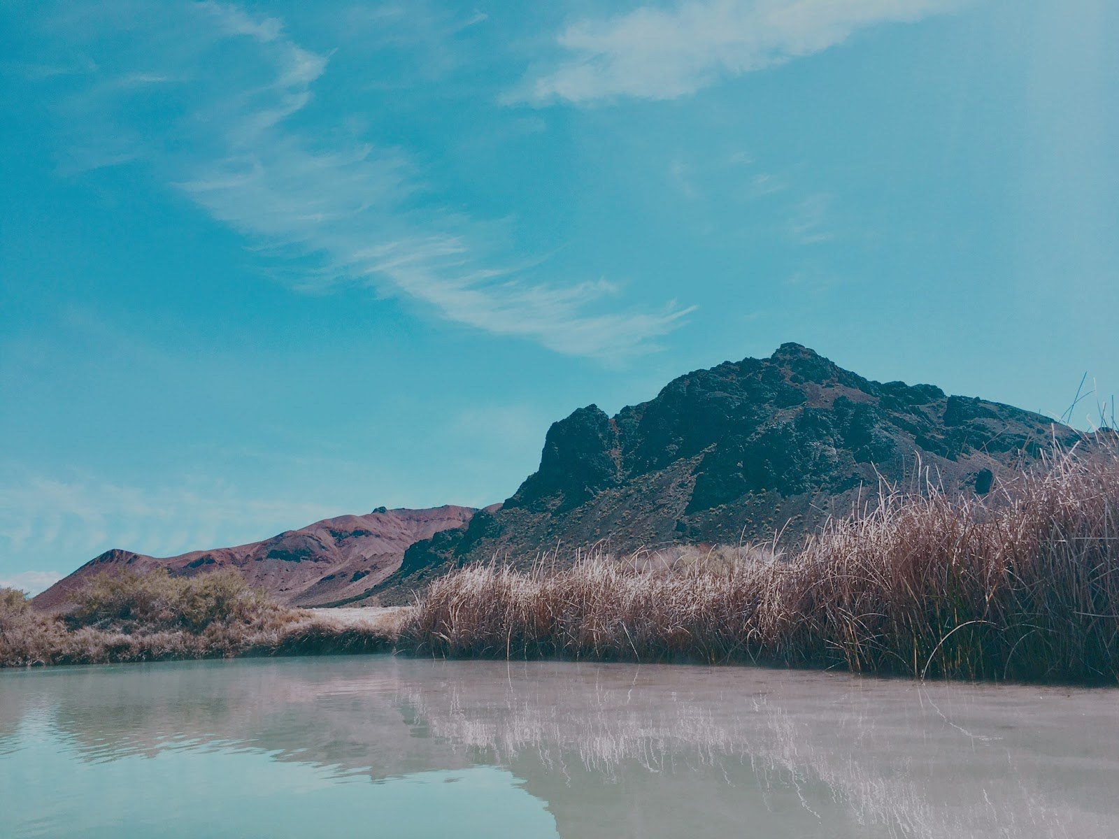 Natural steaming pool at Black Rock Hot Springs with dry grass and rugged mountain under clear blue sky near Gerlach, Nevada