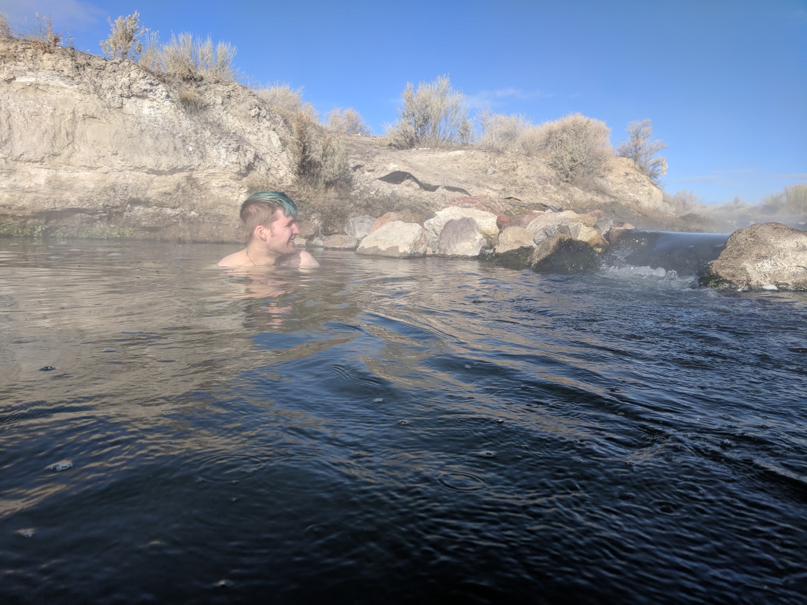 Individual soaking in steamy waters of Bog Hot Springs, surrounded by rocky banks and dry vegetation near Denio, Nevada