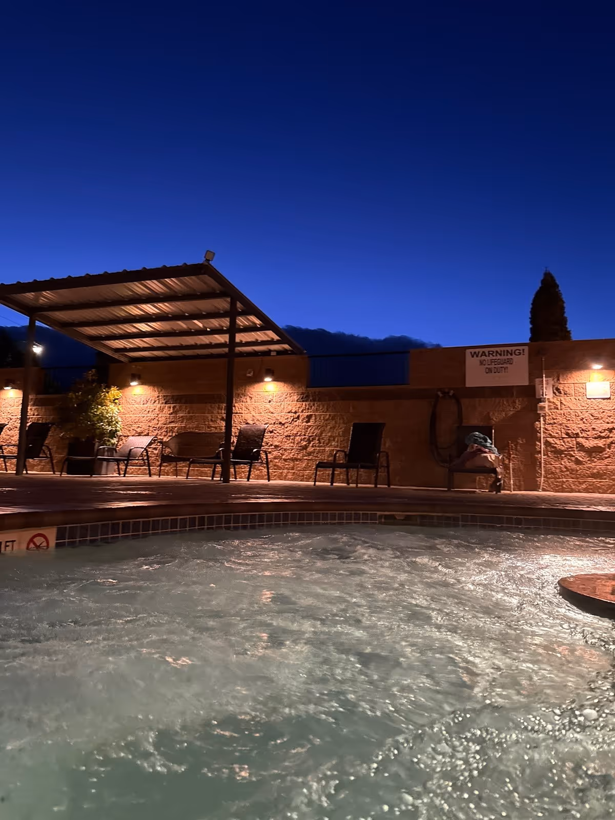 Evening view of the tranquil outdoor spa pool at Carson Hot Springs, Nevada, with seating and a clear dark blue sky above.
