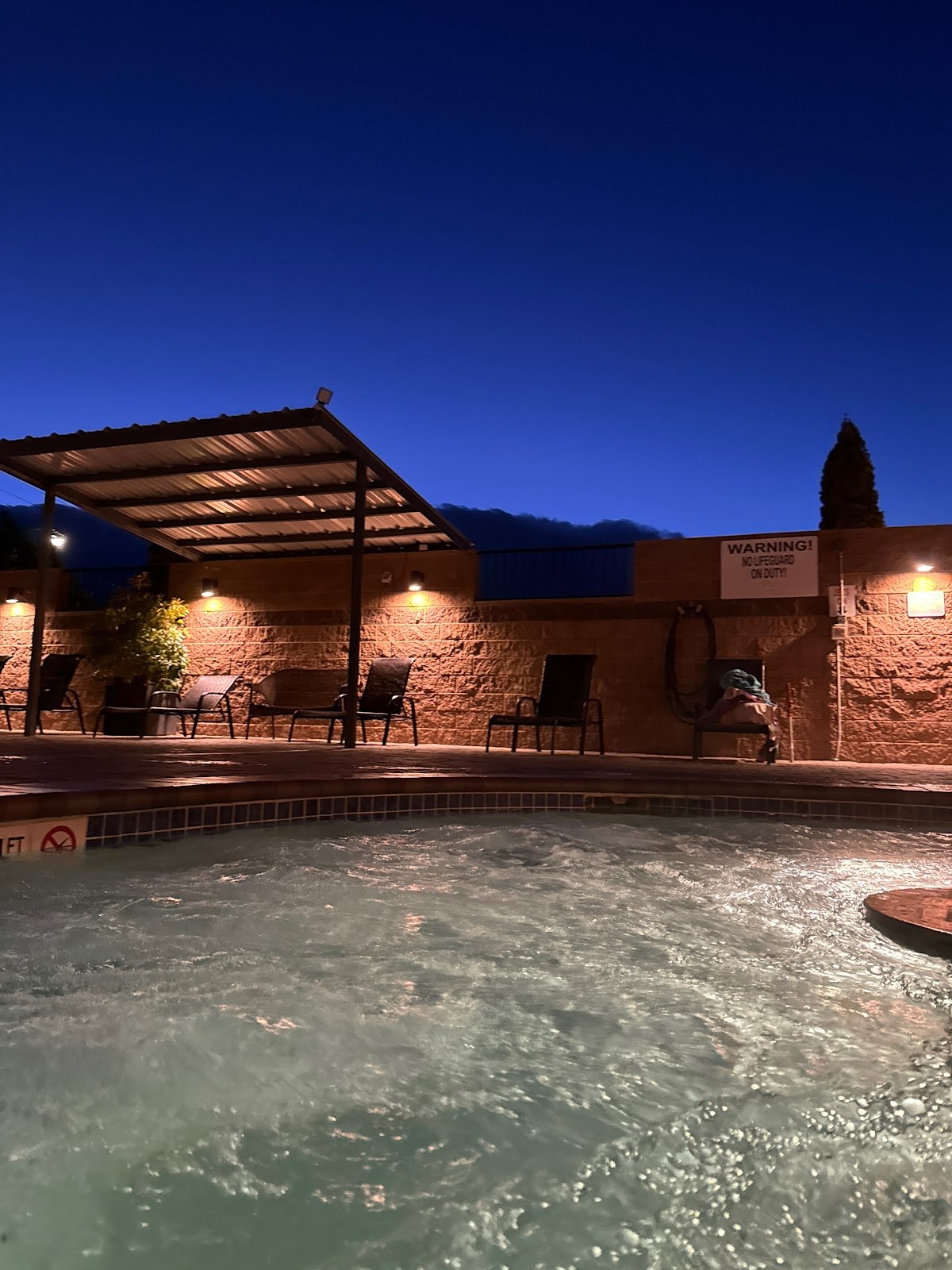 Evening view of the tranquil outdoor spa pool at Carson Hot Springs, Nevada, with seating and a clear dark blue sky above.