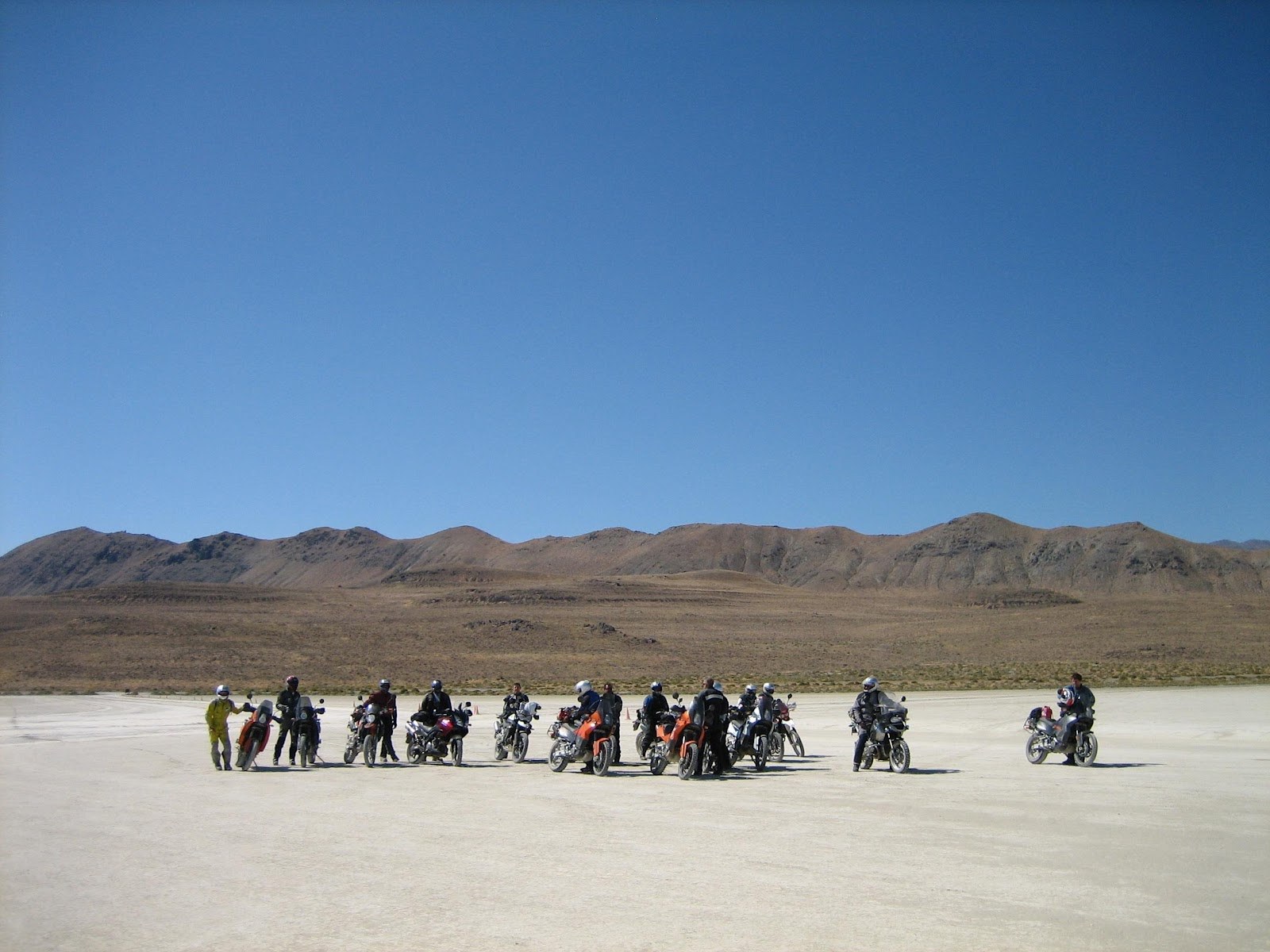 Group of motorcyclists gathered on a dry flatland with mountainous terrain under a bright sky near Gerlach, Nevada, United States