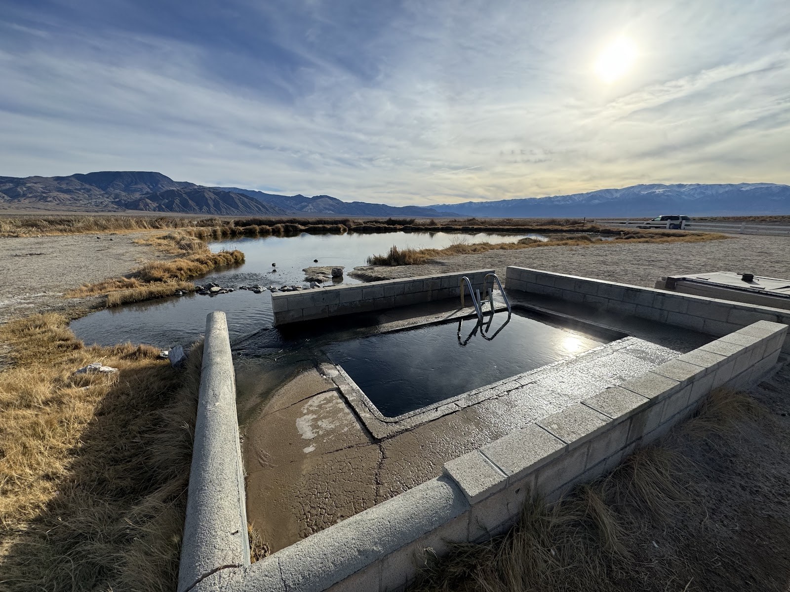 Outdoor rectangular spa pool filled with water at Fish Lake Valley Hot Well near Dyer, Nevada, surrounded by open plains and distant mountains.
