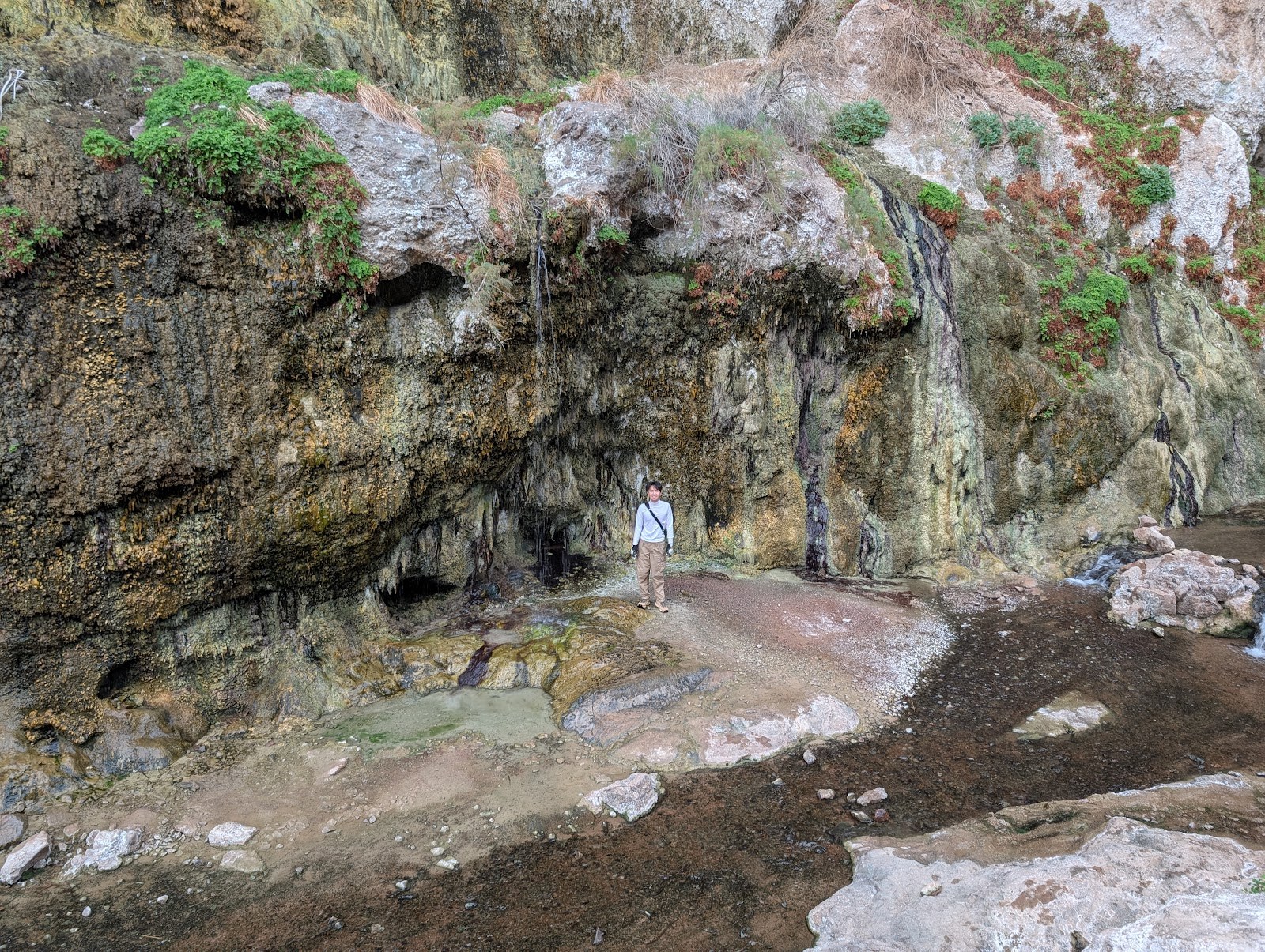 Person standing inside a mineral spring cave with colorful rock formations and water flow at Gold Strike Hot Springs, Nevada.