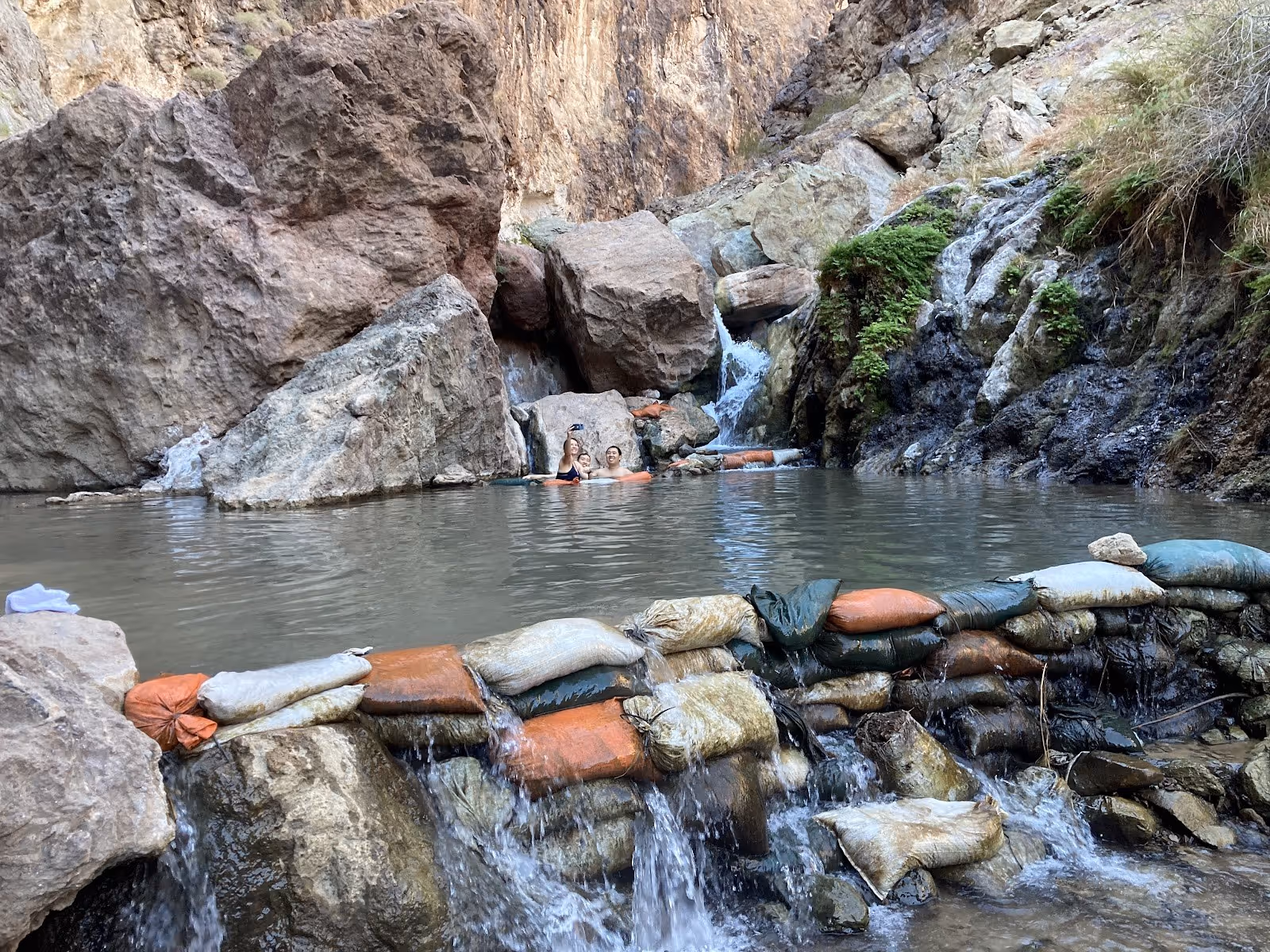 Two people soaking in a natural hot spring pool at Gold Strike Hot Springs near Boulder City, Nevada with rocky surroundings.
