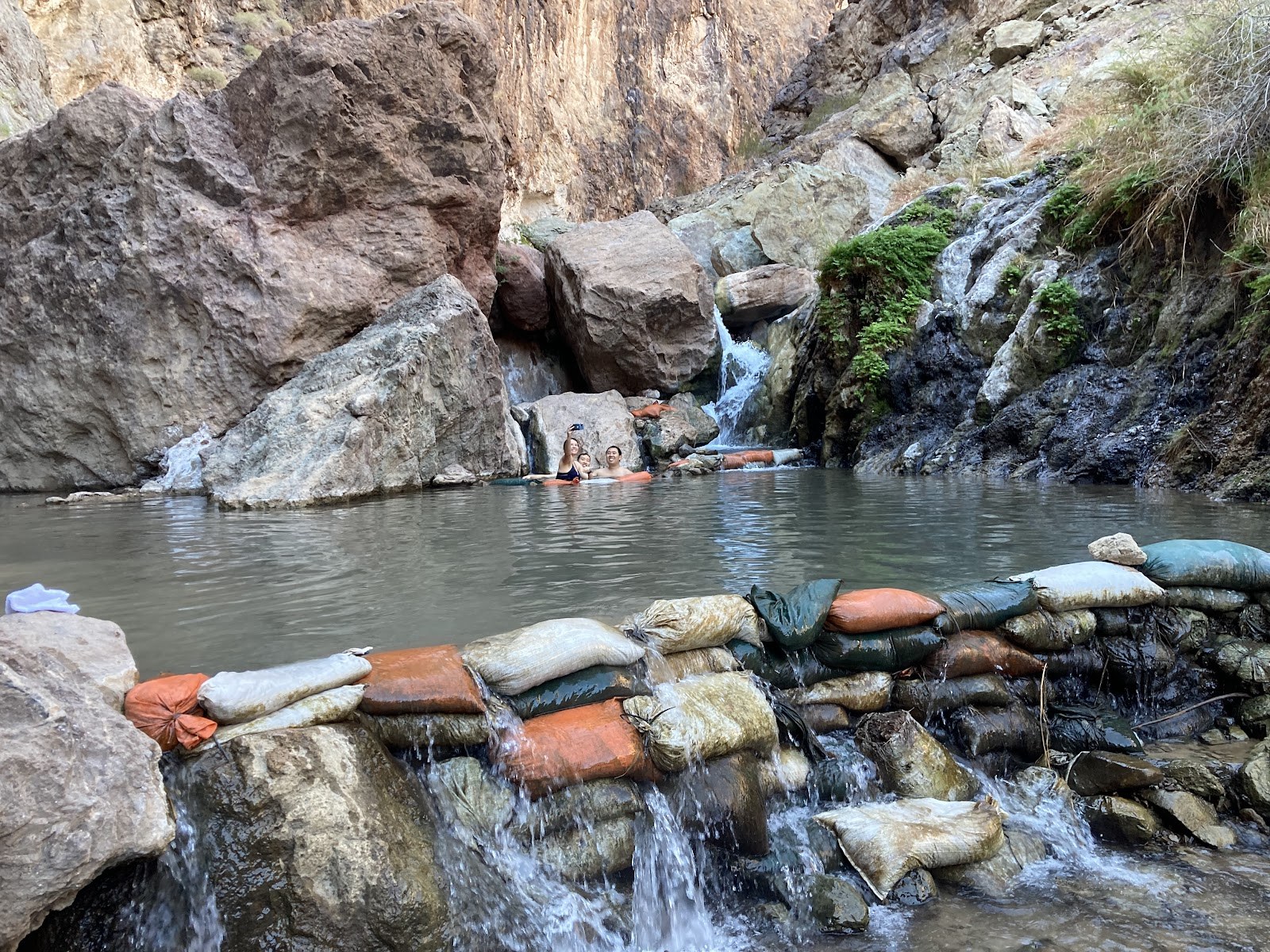 Two people soaking in a natural hot spring pool at Gold Strike Hot Springs near Boulder City, Nevada with rocky surroundings.
