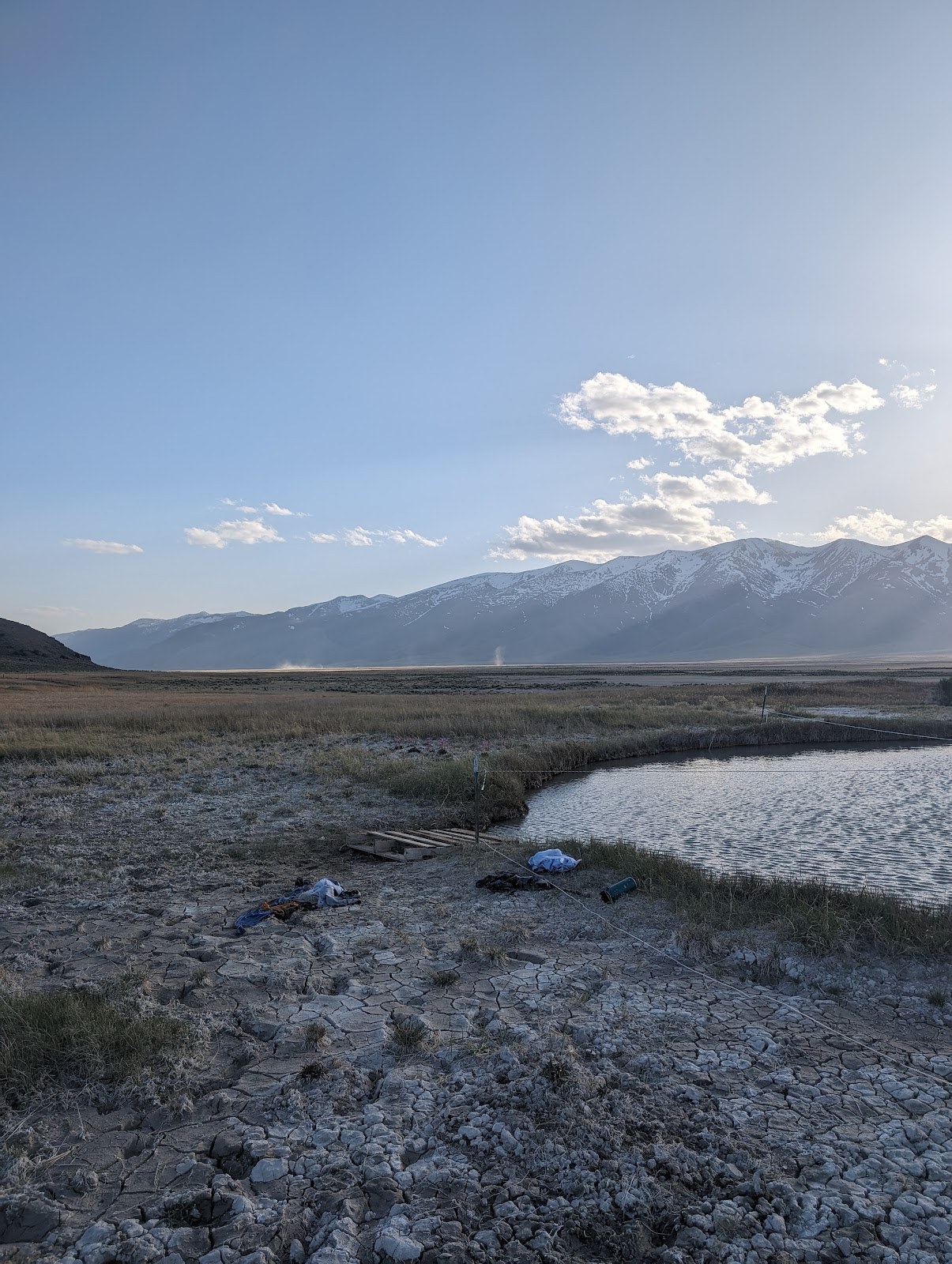 Ruby Valley Hot Springs natural pool with steam rising in the distance and dry cracked earth in the foreground, near Elko, Nevada