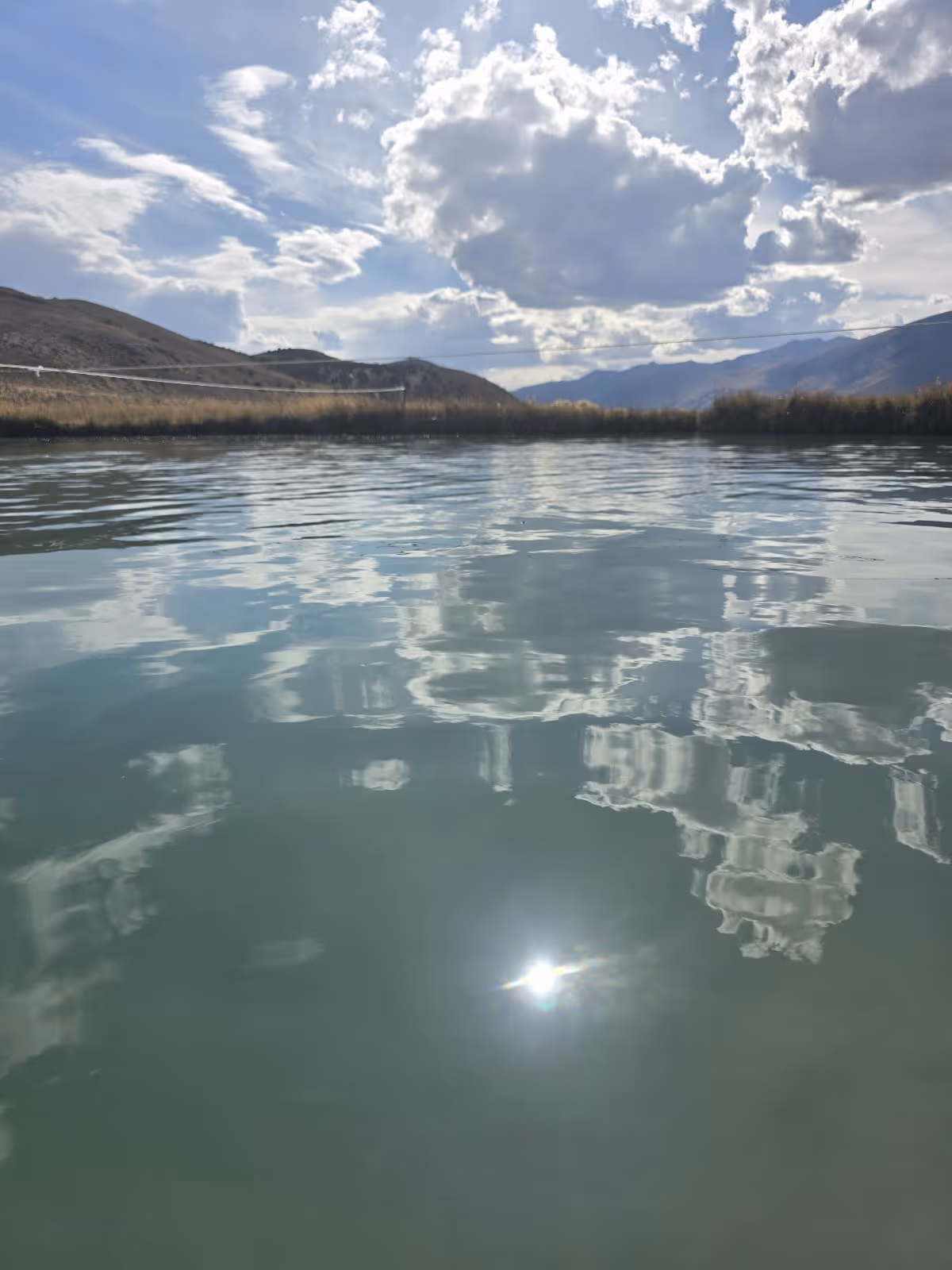 Close-up of water surface at Ruby Valley Hot Springs with reflections of clouds and sun, located near Elko, Nevada