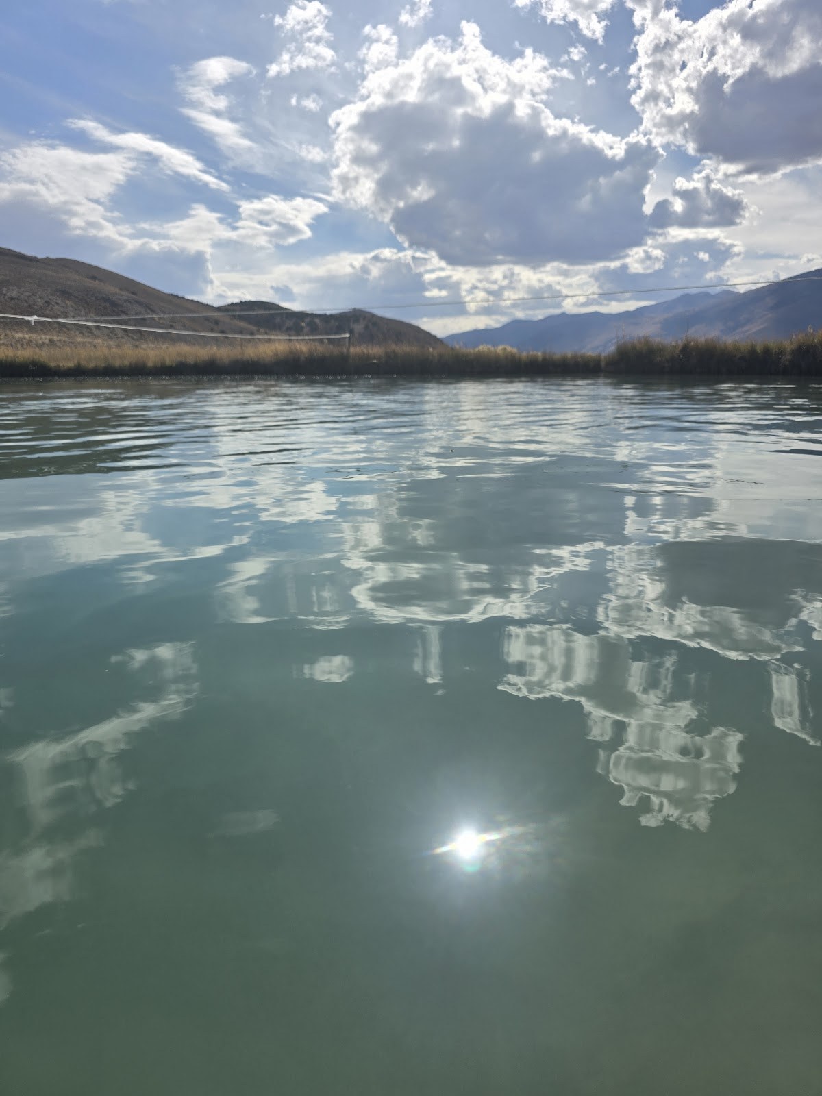 Close-up of water surface at Ruby Valley Hot Springs with reflections of clouds and sun, located near Elko, Nevada