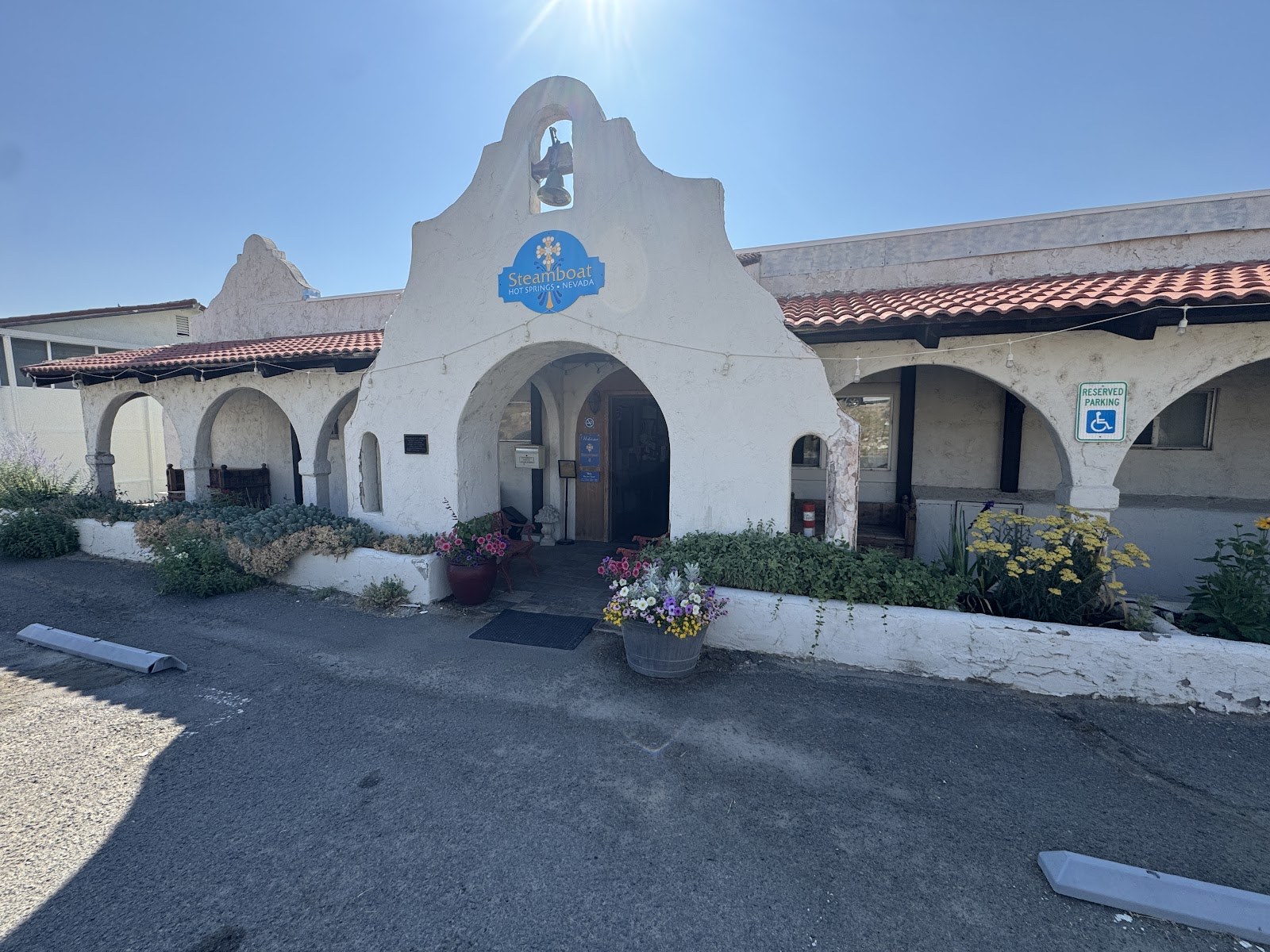 White stucco building entrance of Steamboat Hot Springs Healing Center & Spa near Reno, Nevada with a blue sign and decorative flowers in front