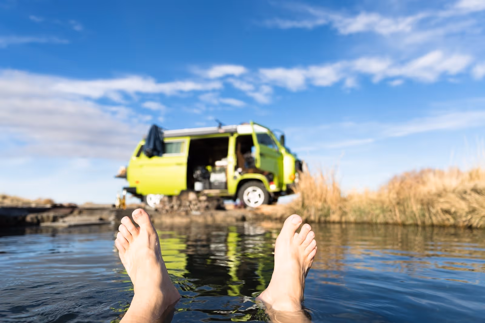 View of feet soaking in Trego Hot Springs pool near Gerlach, Nevada, with a yellow van and dry grass under blue sky.