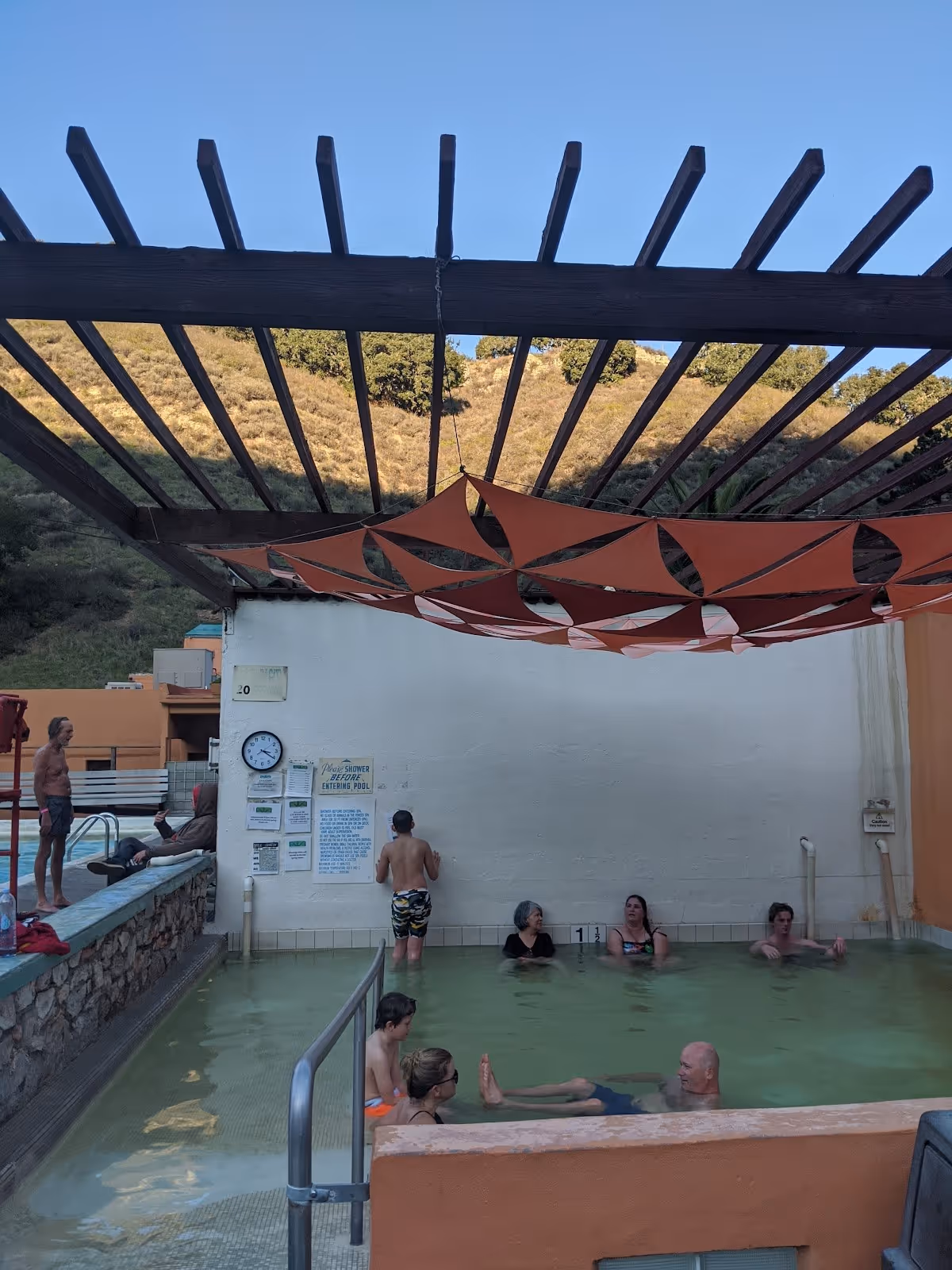Indoor mineral hot spring pool at Avila Hot Springs with people soaking and a shaded beam structure overhead in California.