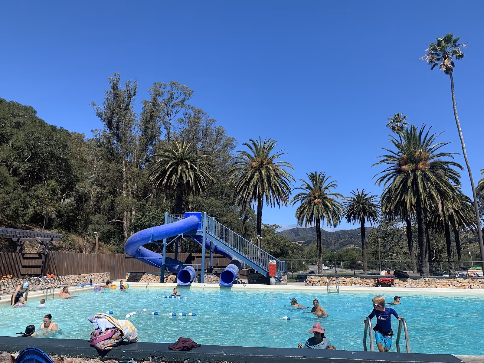 Outdoor pool at Avila Hot Springs in California with blue water slides and palm trees under a clear blue sky near Avila Beach.