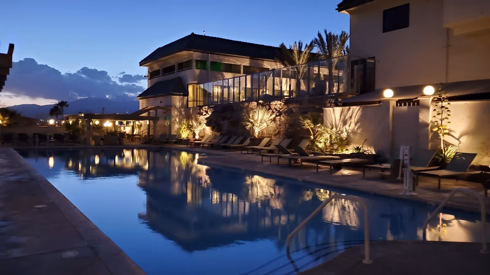 Azure Palm Hot Springs outdoor pool lit by evening lights with a building and mountains visible in Desert Hot Springs California.