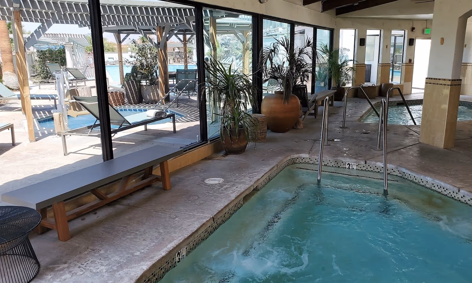 Indoor spa pool with bubbling water and steam at Azure Palm Hot Springs featuring plants and large windows overlooking the outdoor area.