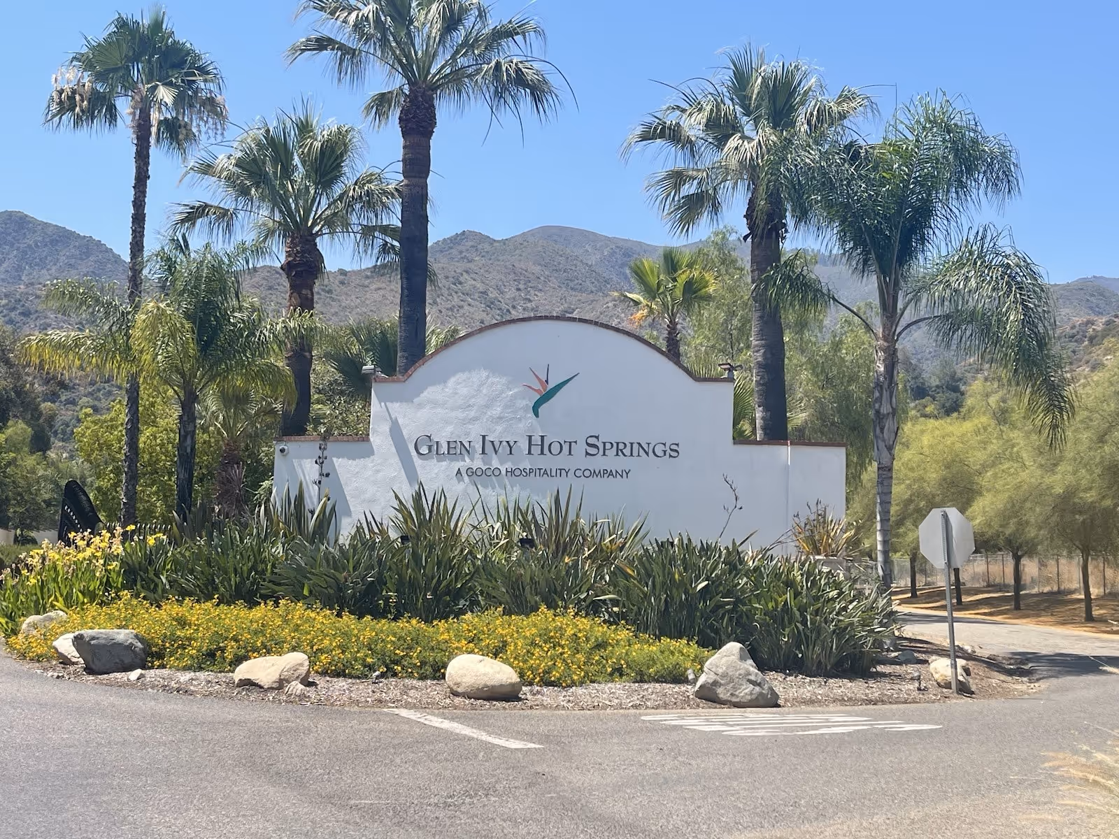 Entrance sign for Glen Ivy Hot Springs in Temescal Valley California with landscaping and palm trees against a backdrop of hills.