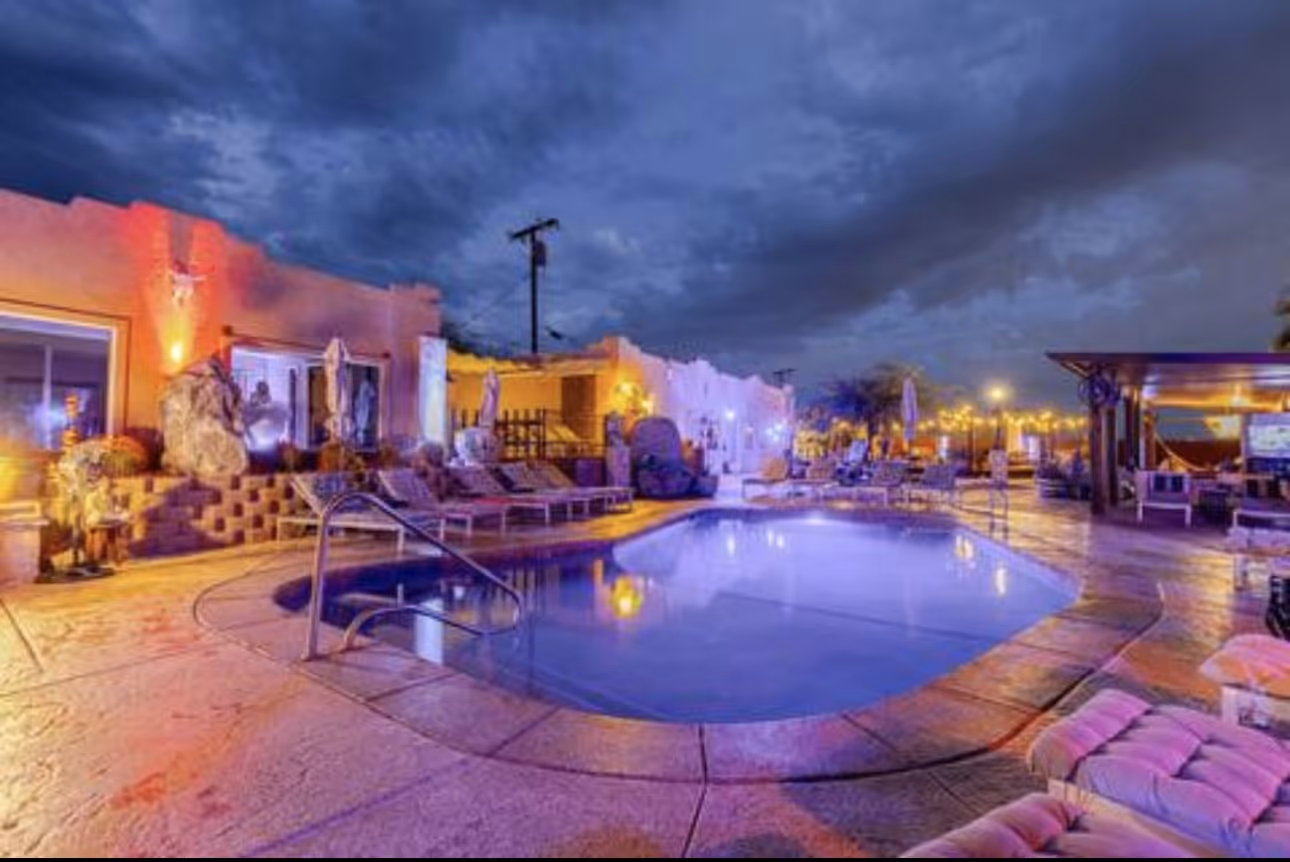 Dusk at Mi Kasa Hot Springs with illuminated outdoor hot spring pool, soft lounge chairs, and a cloudy sky in Desert Hot Springs California.
