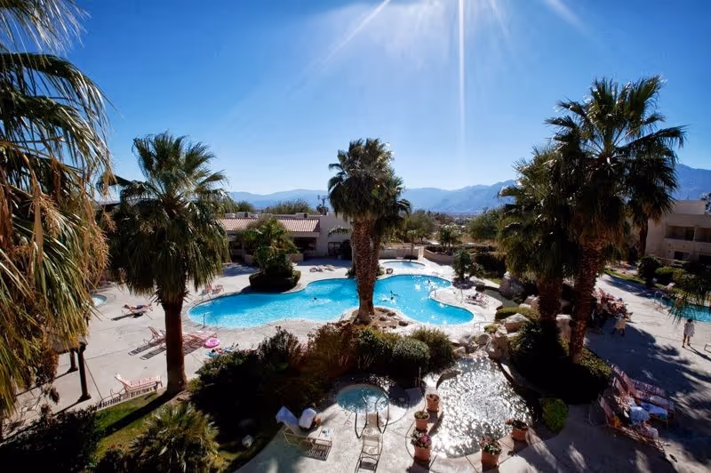 Aerial view of mineral soaking pools and palm trees at Miracle Springs Resort with desert mountains in the background near Desert Hot Sprin.