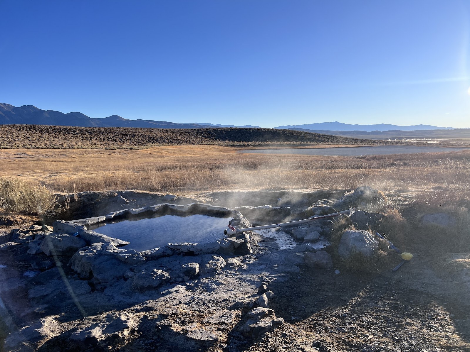 Shepherd Hot Springs natural soaking pool with stone border steaming in dry grassy meadow near Mammoth Lakes california.