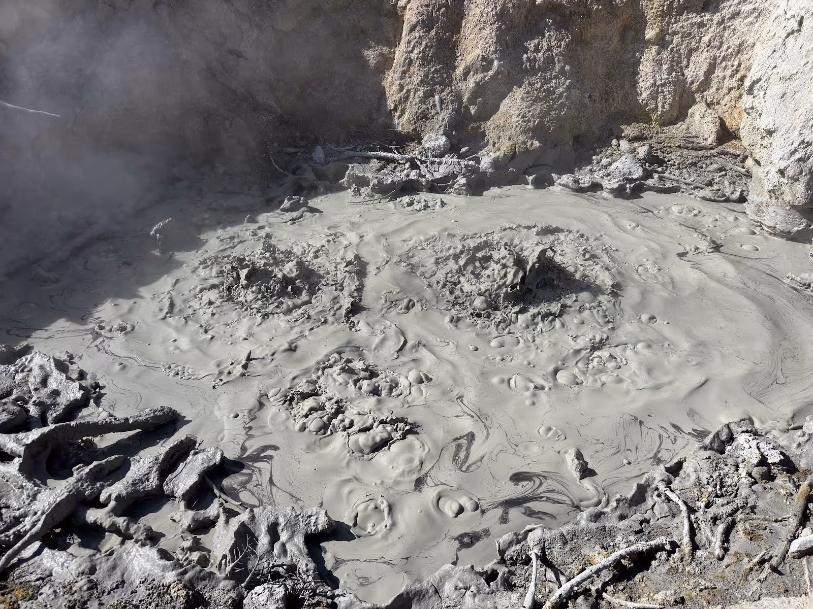 Gray bubbling mud pool with rising steam surrounded by rocky terrain at Sulphur Works near Mineral, California.