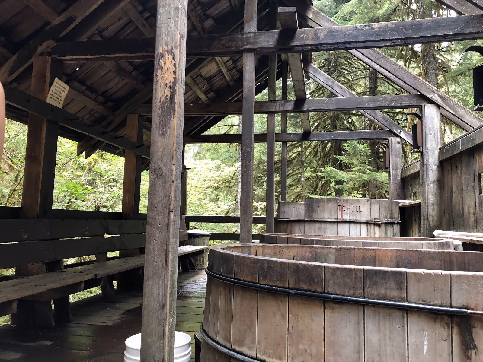 Several wooden soaking tubs under a covered shelter surrounded by dense forest at Bagby Hot Springs in Oregon.