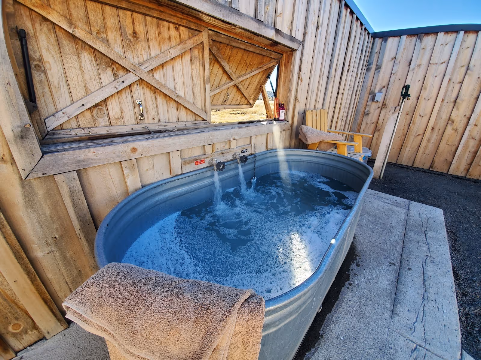 Metal private soaking tub filling with bubbling water surrounded by wooden fence and chair at Crystal Crane Hot Springs Oregon.
