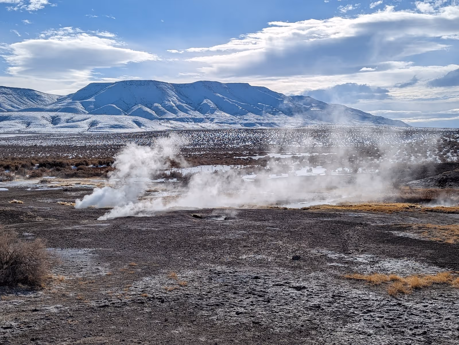 Steam rising from vents across the rocky ground of Mickey Hot Springs with snowy mountains in the background near Burns Oregon.