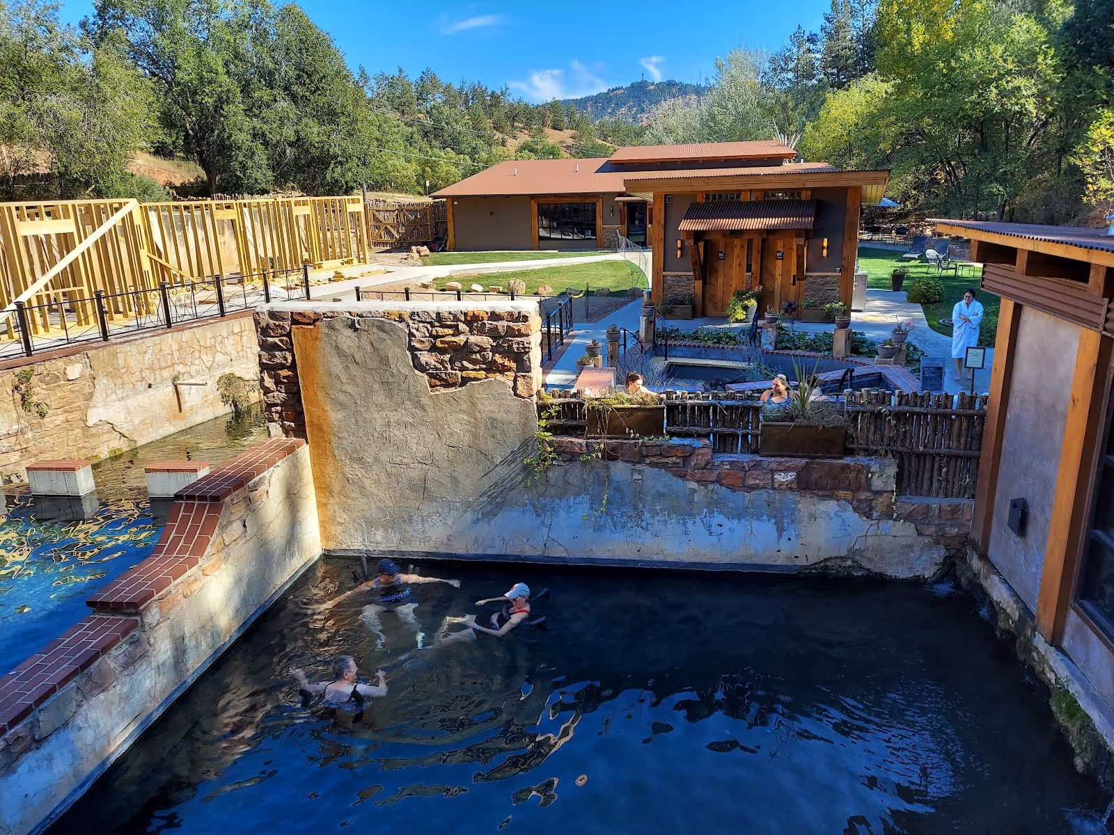 Several people soaking in a dark water hot spring pool at Moccasin Springs Natural Mineral Spa in Hot Springs South Dakota with spa buildin.