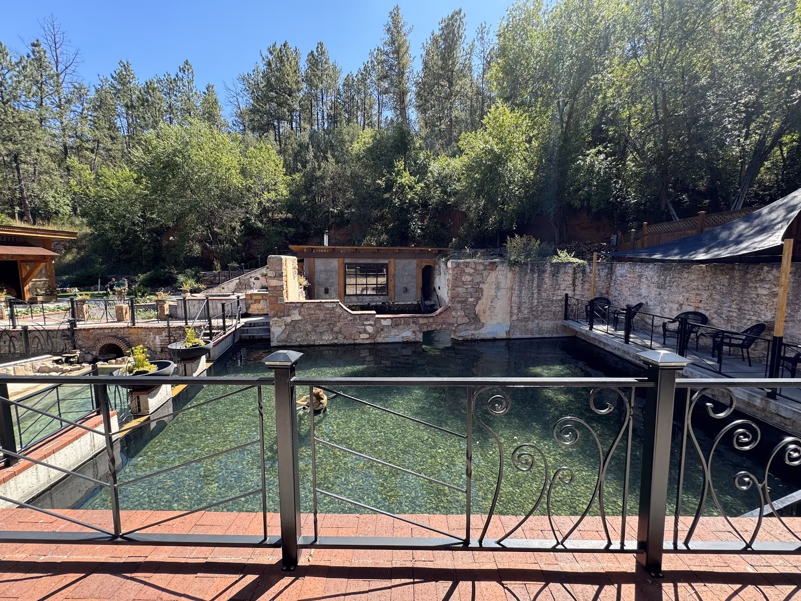 Large fenced natural hot spring pool at Moccasin Springs in Hot Springs South Dakota with clear water and surrounding trees on a sunny day.