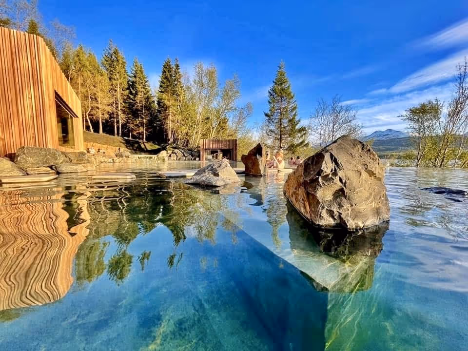 Clear mineral pool at Forest Lagoon featuring large rocks and people soaking surrounded by forest and mountains.
