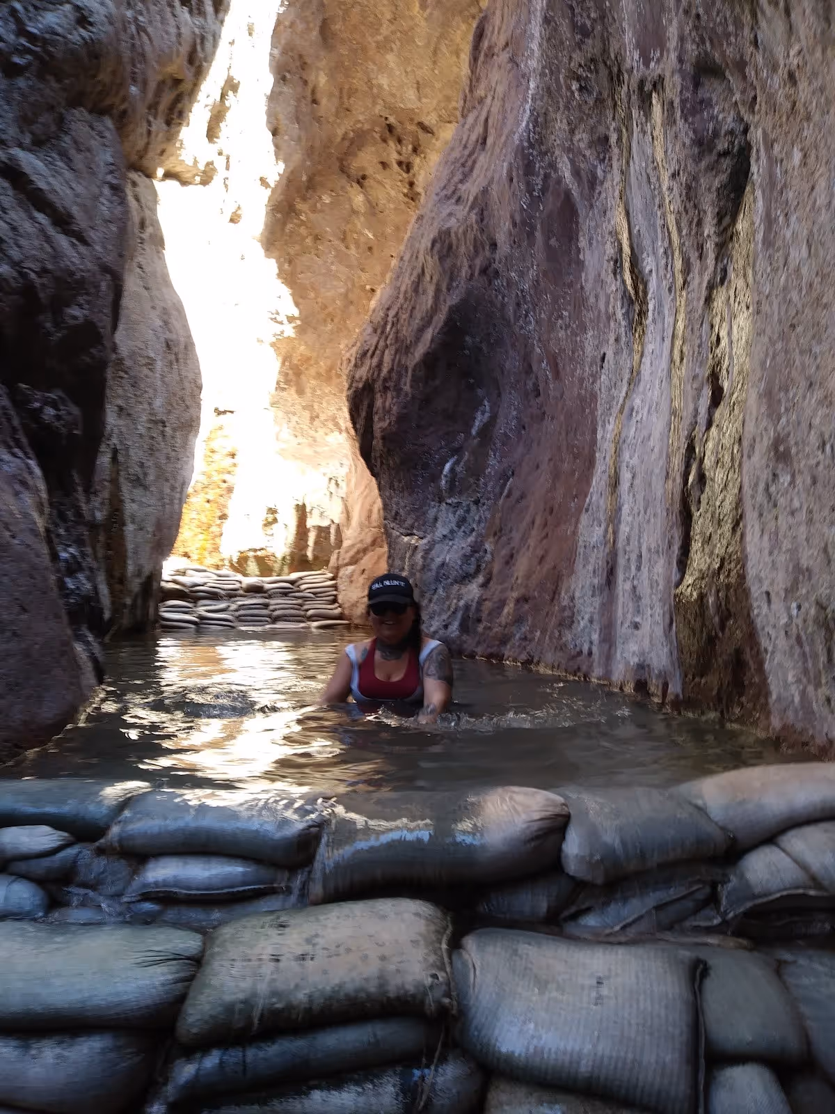 A person wearing a hat relaxes in a mineral pool held by sandbags inside a narrow canyon at Arizona Hot Springs, united states.