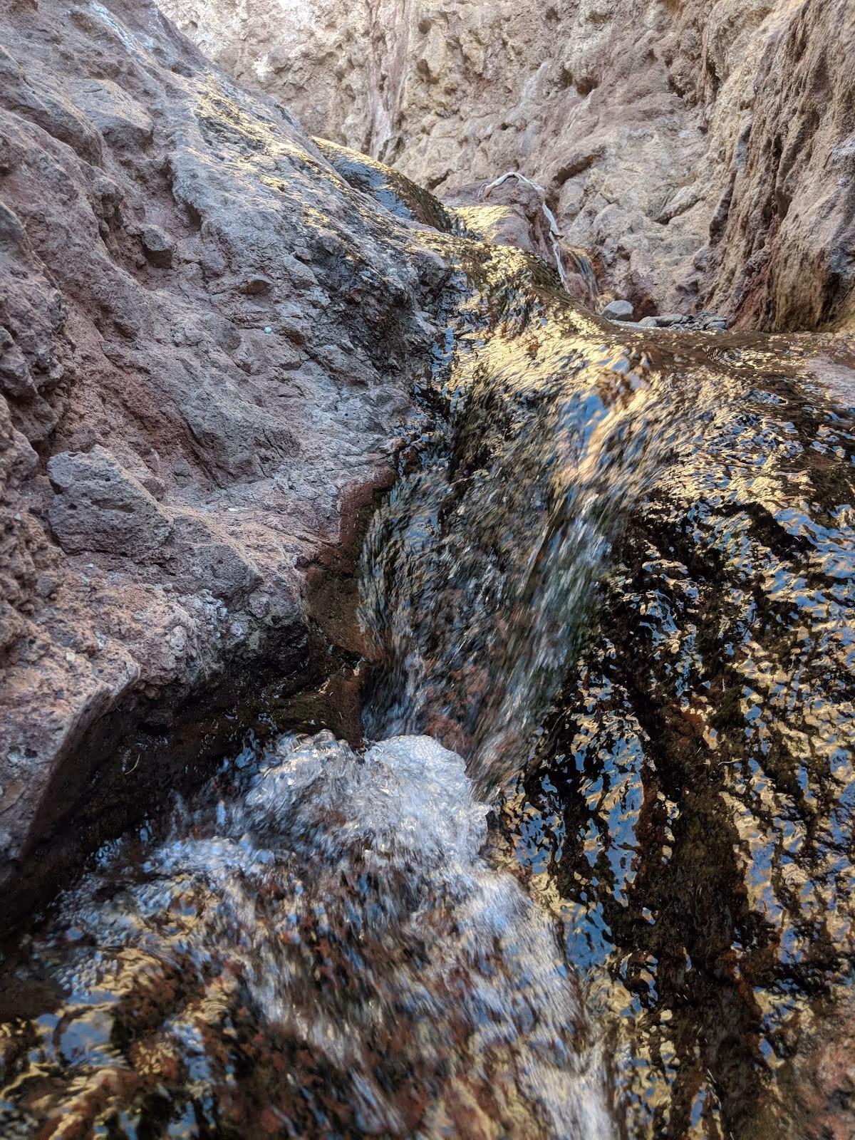Close-up view of clear water flowing over dark, wet rocks forming a small stream within the rocky canyon of Boy Scout Hot Springs.