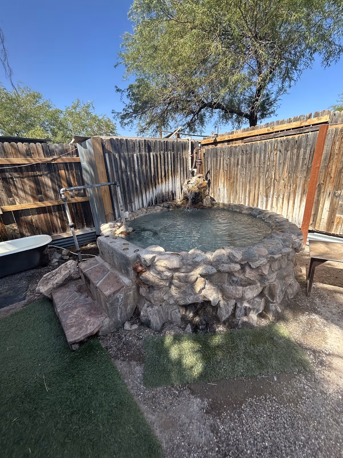 Small round stone soaking pool with handrails and wooden fence enclosure at El Dorado Hot Springs in Arizona.