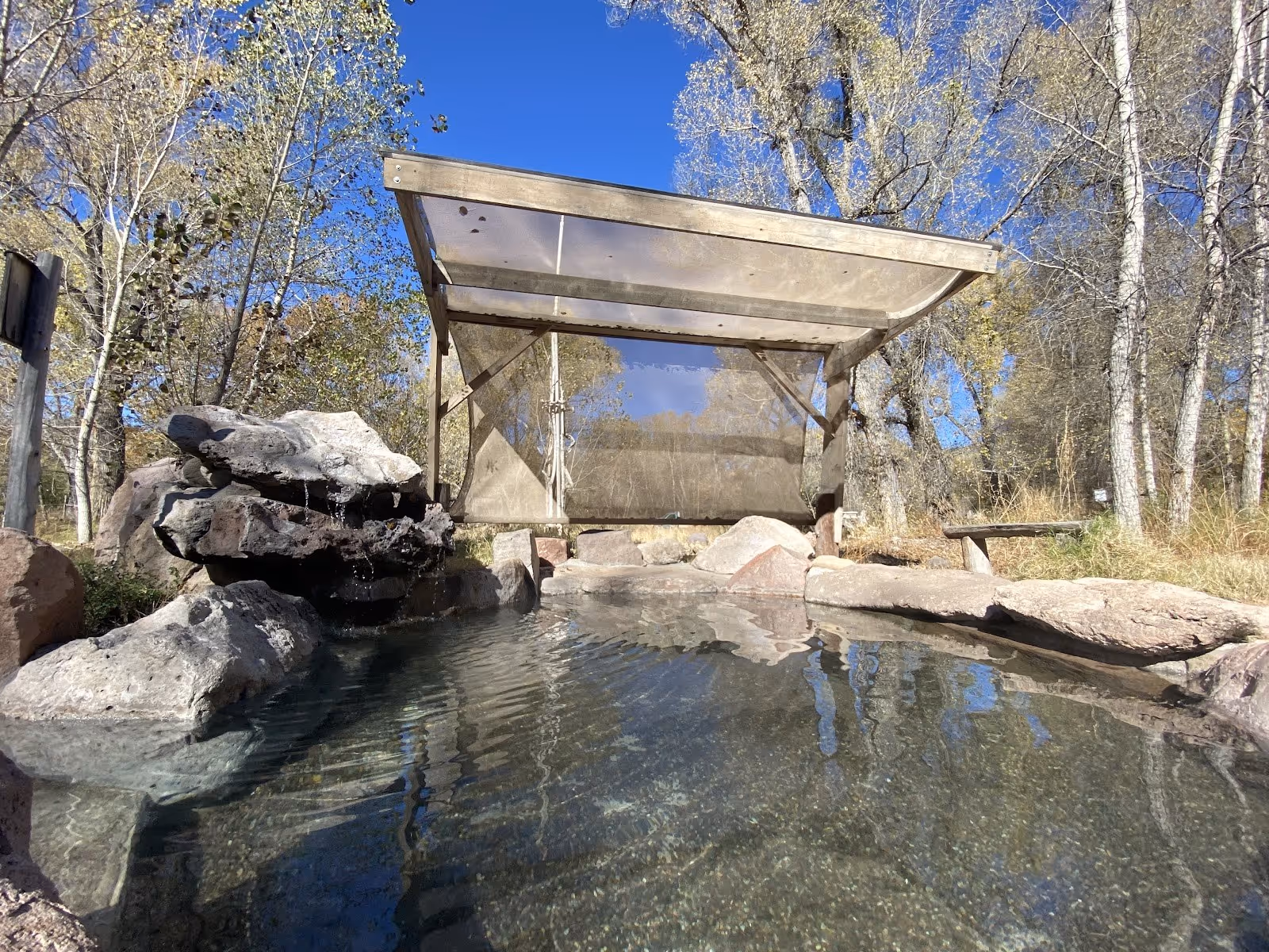 Clear water in an outdoor hot spring pool at Gila Hot Springs Campground with rocks and leafless trees near Silver City New Mexico.