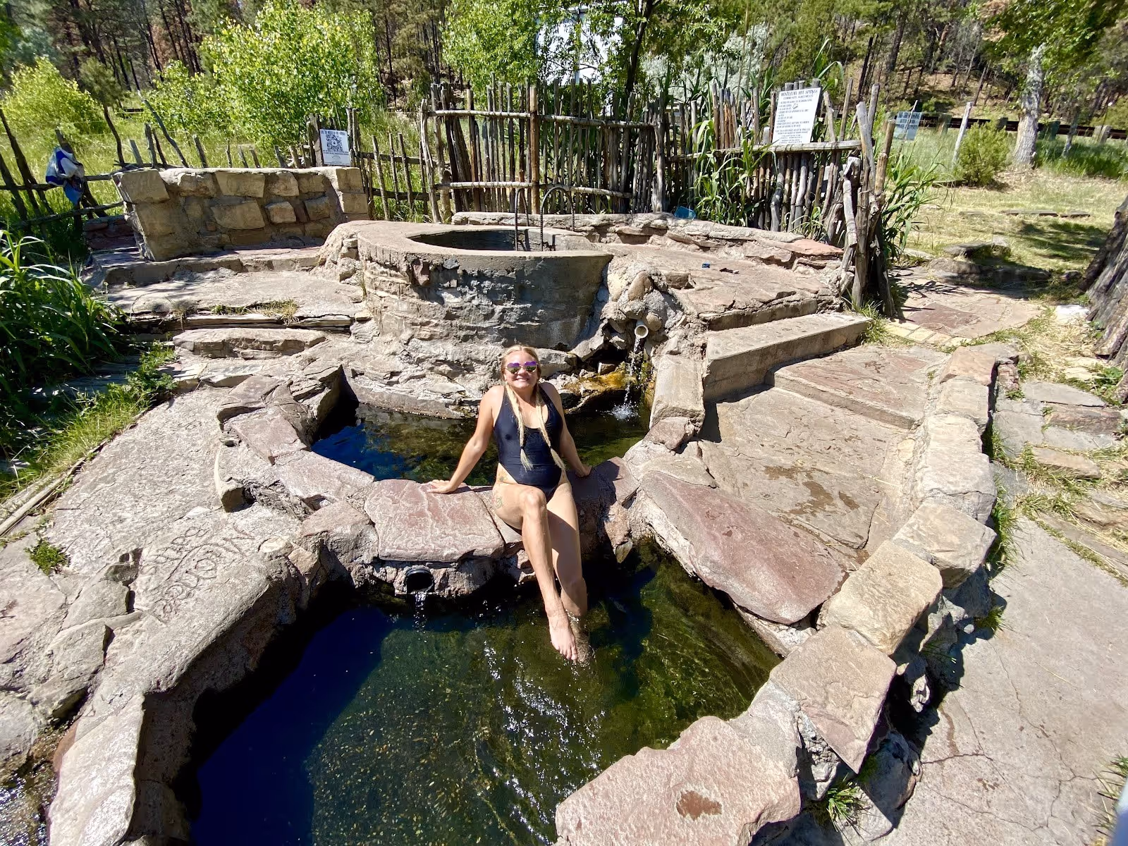 A woman relaxing in a stone outdoor hot spring pool at Montezuma Hot Springs near Las Vegas New Mexico with greenery in the background.