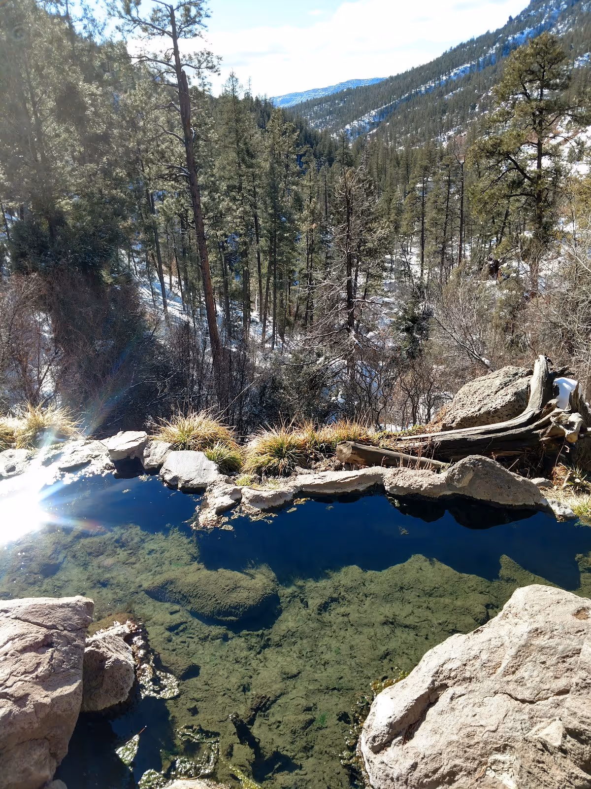Clear natural hot spring pool at Spence Hot Spring with rocky edges and tall pine trees in the background near Jemez Springs New Mexico.