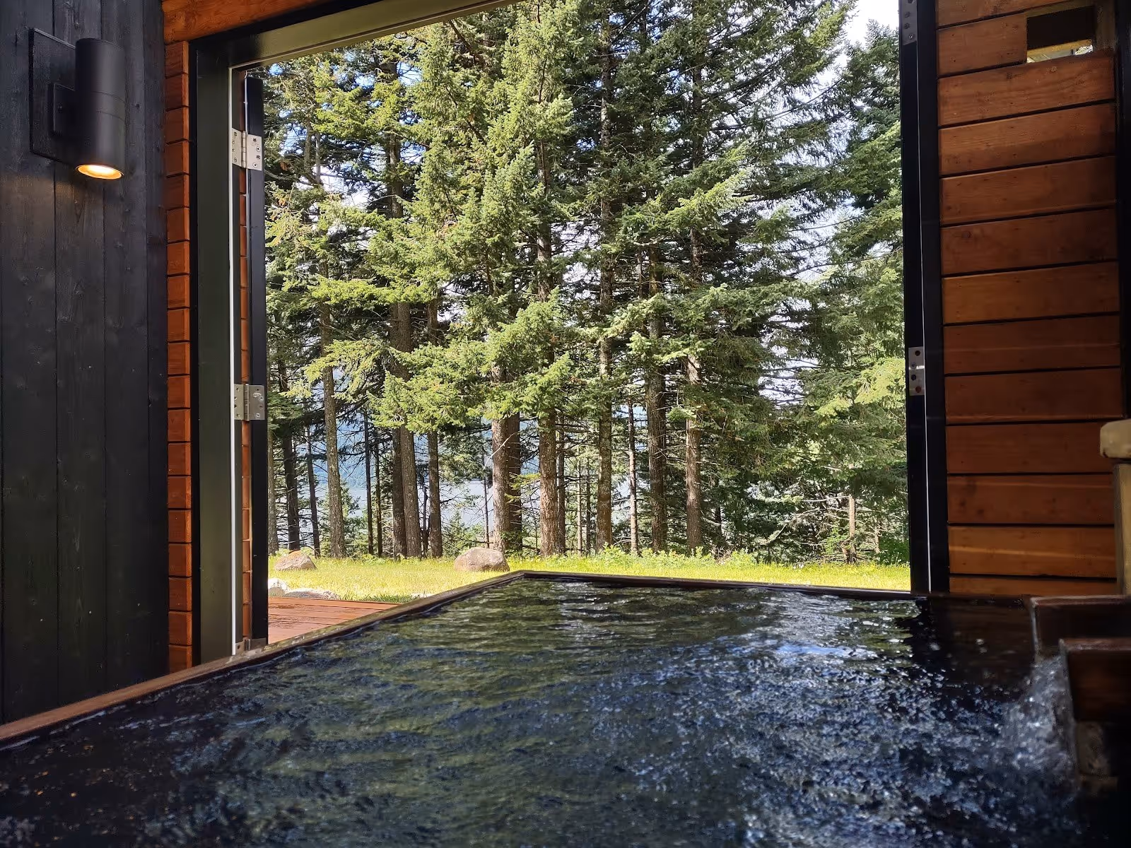 Indoor hot spring soaking pool at Tenzen Springs with open sliding doors revealing tall pine trees outside near Stevenson Washington.