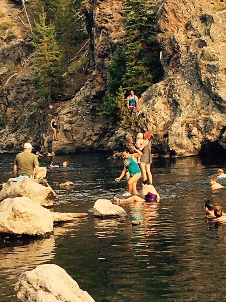 People relaxing and swimming near large rocks and steep cliffs at Firehole River Swimming Area, a hot spring pool near West Yellowstone.