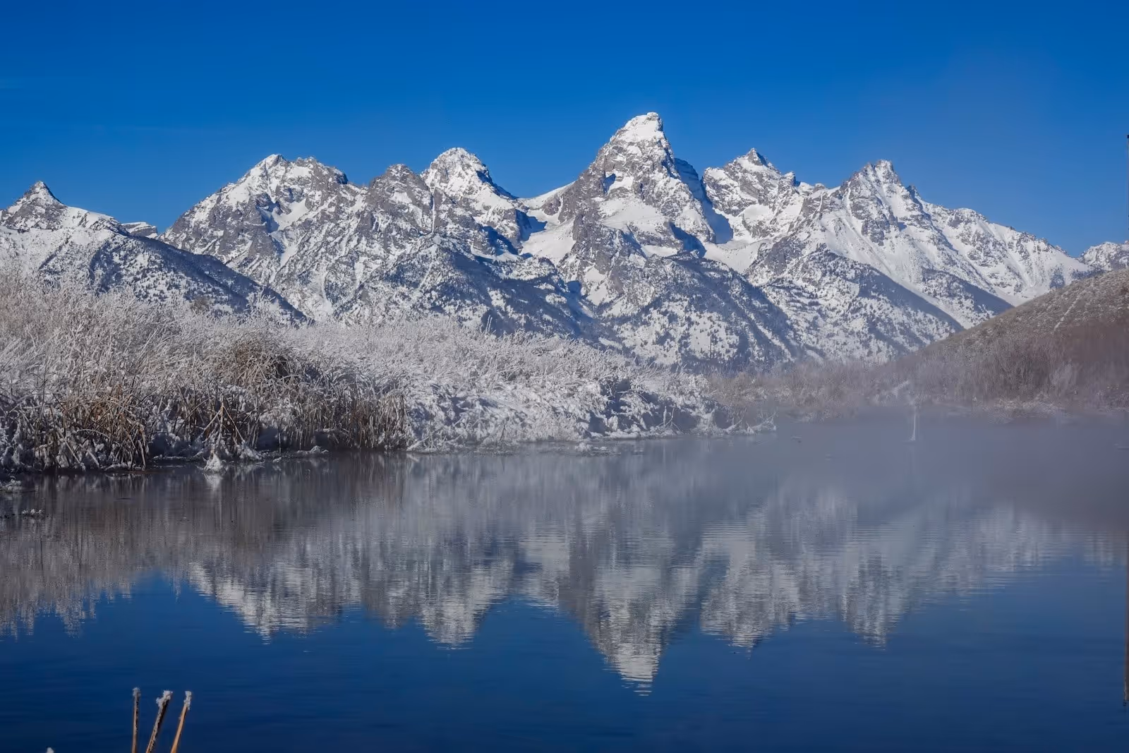 Calm natural hot spring pond at Kelly Hot Springs reflecting snow-capped mountain peaks near Kelly, Wyoming.