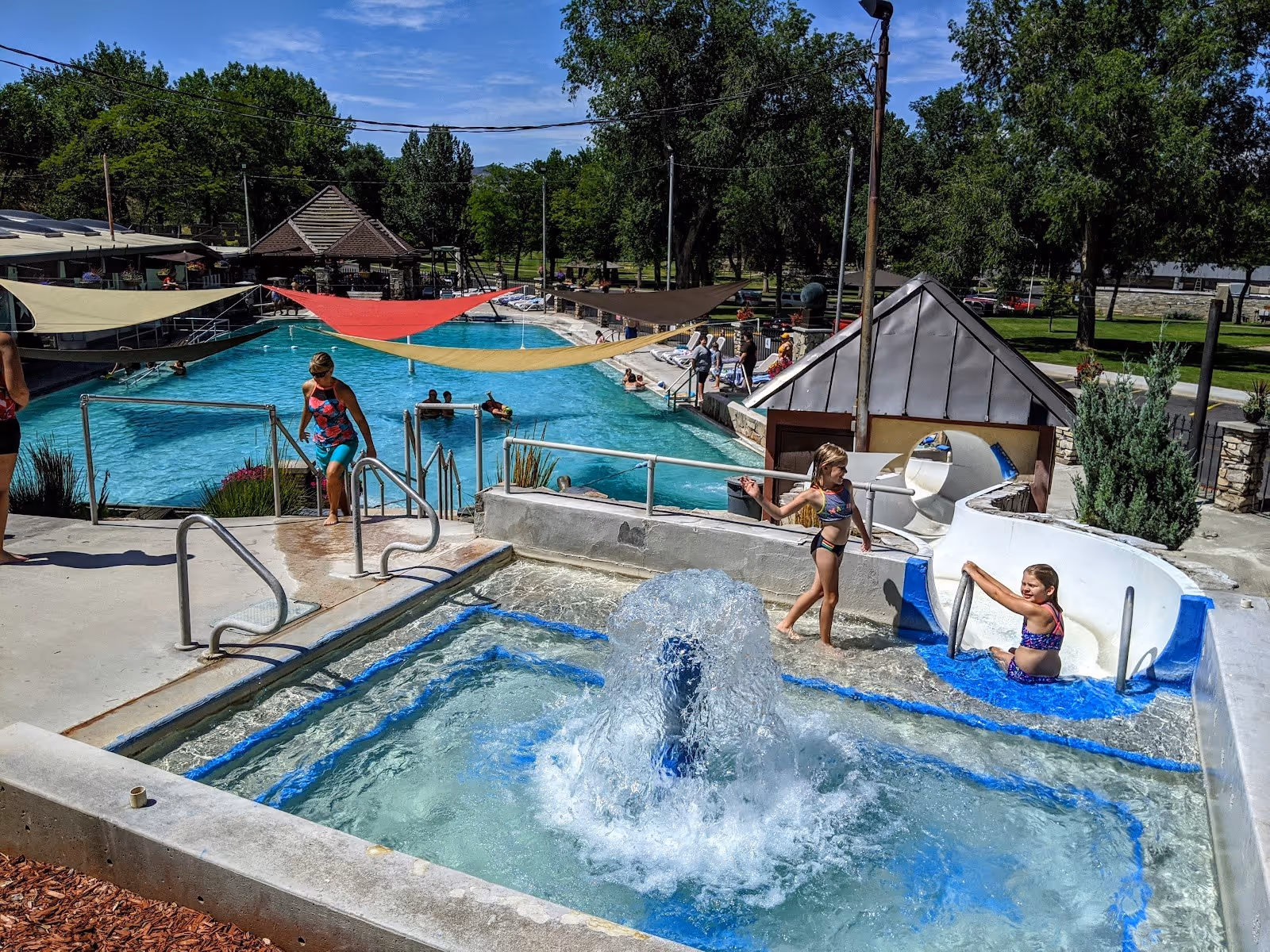 Children play near water features including a bubbling fountain and a slide by the outdoor mineral pool at Star Plunge in Thermopolis Wyomi.