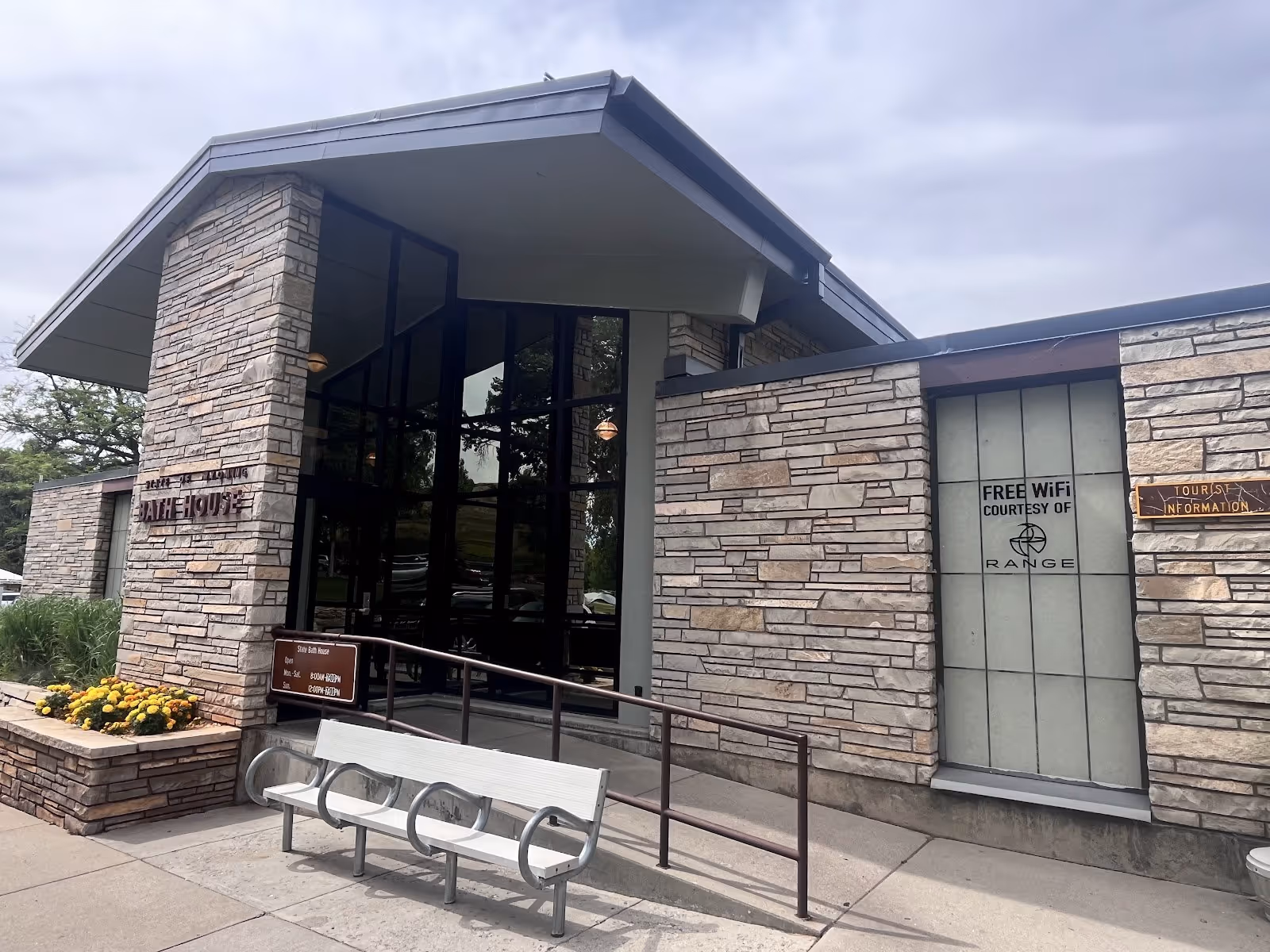 Entrance to State Bath House in Thermopolis Wyoming showing stone facade, glass doors, bench, and signs for WiFi and tourist information.