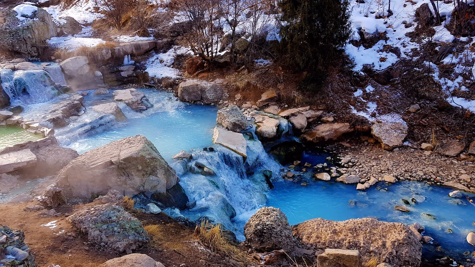 Natural hot spring pools at Fifth Water Hot Springs surrounded by snow and steam in mountainous terrain near Spanish Fork Utah.