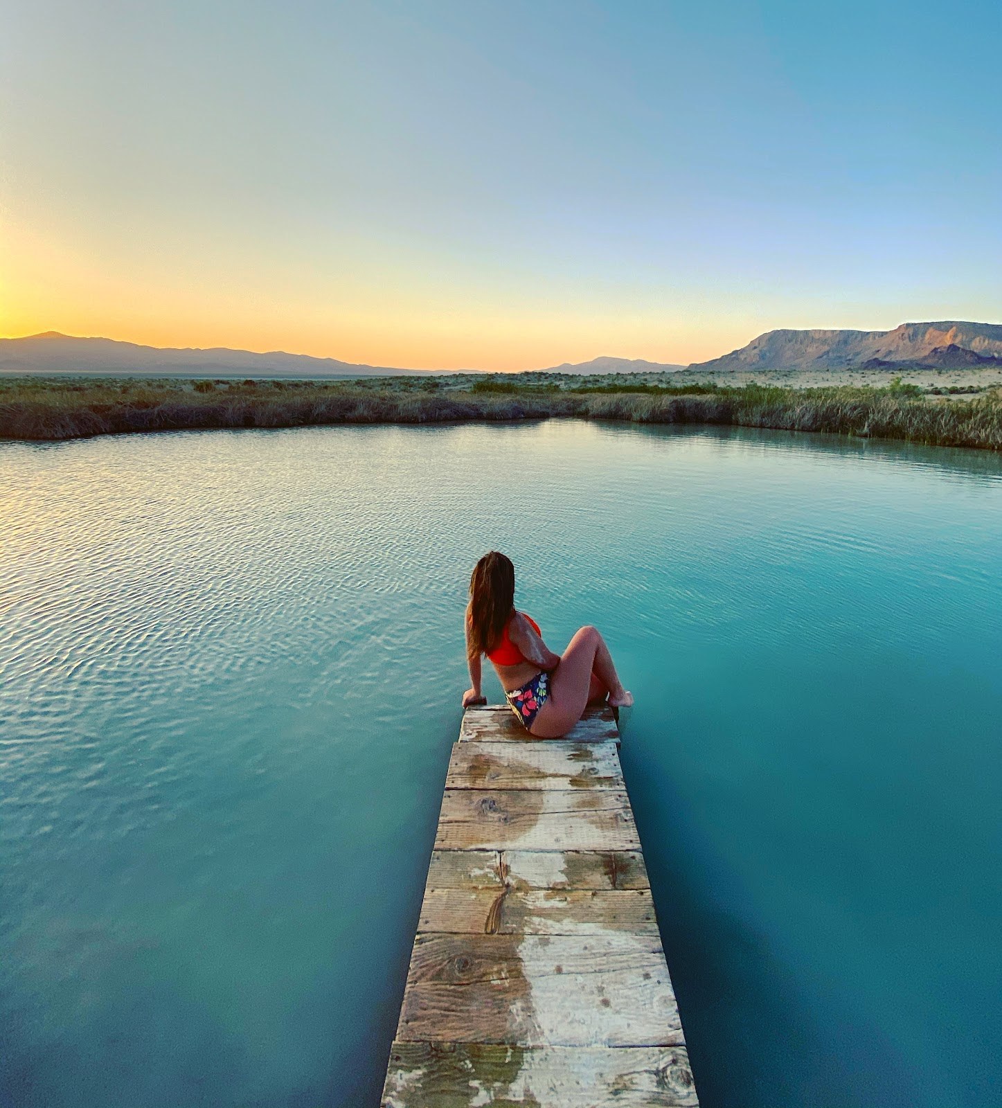 Wooden dock extending into blue waters of Black Rock Hot Springs with steam and distant mountainous horizon near Gerlach, Nevada