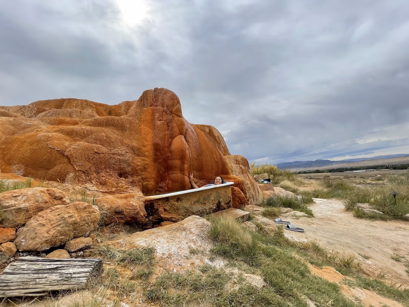 Outdoor soaking tub built next to an orange travertine mound at Monroe Hot Springs with a person relaxing inside the water.