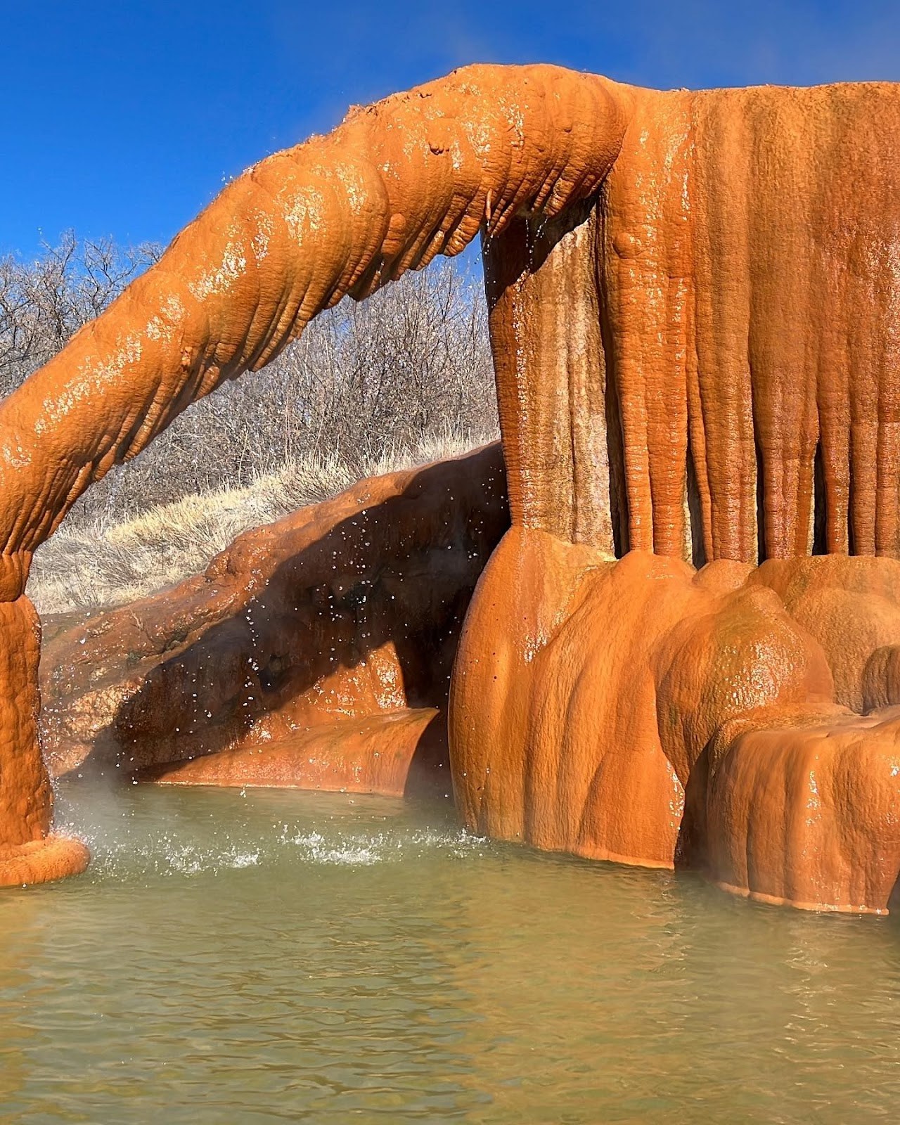 Travertine formation arch with orange mineral deposits over flowing water and steam at Monroe Hot Springs near Monroe Utah.