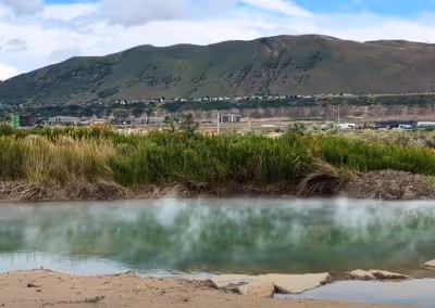 Steaming outdoor hot spring pool at Mountain Point Lake with green grasses and hills near Bluffdale, Utah.