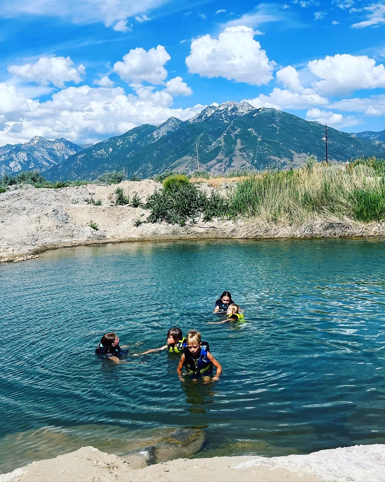 Several children wearing life jackets swimming in a natural pool at Mountain Point Lake with a mountain backdrop in Utah.