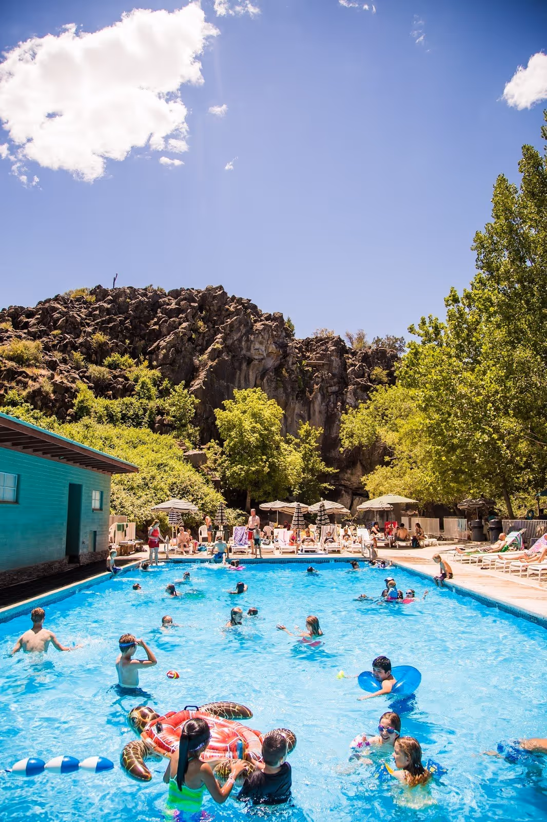 Outdoor pool at Veyo Pool Hot Springs near St. George Utah filled with people swimming on a sunny day under blue sky.