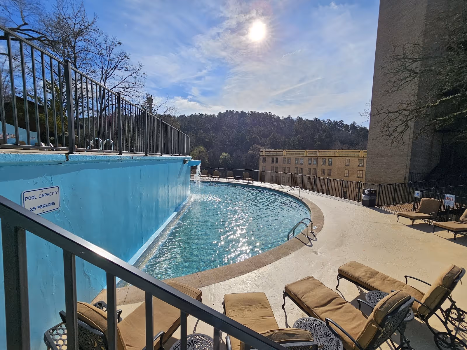 Outdoor hot spring pool at Arlington Resort Hotel & Spa in Hot Springs Arkansas with lounge chairs and a blue wall under sunlight.