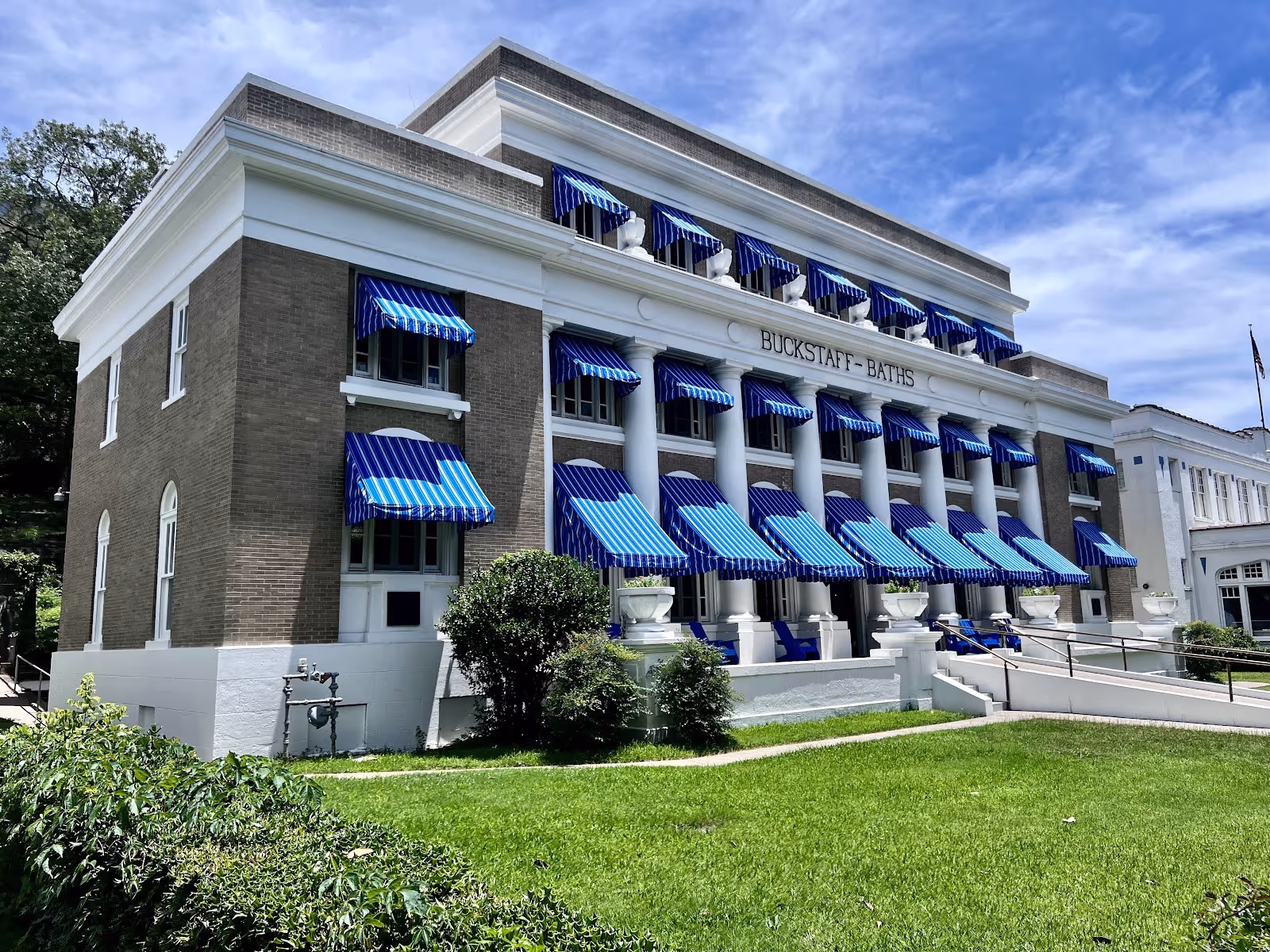 Historic Buckstaff Bathhouse building with large white columns, one side surrounded by green grass and bushes in Hot Springs Arkansas.