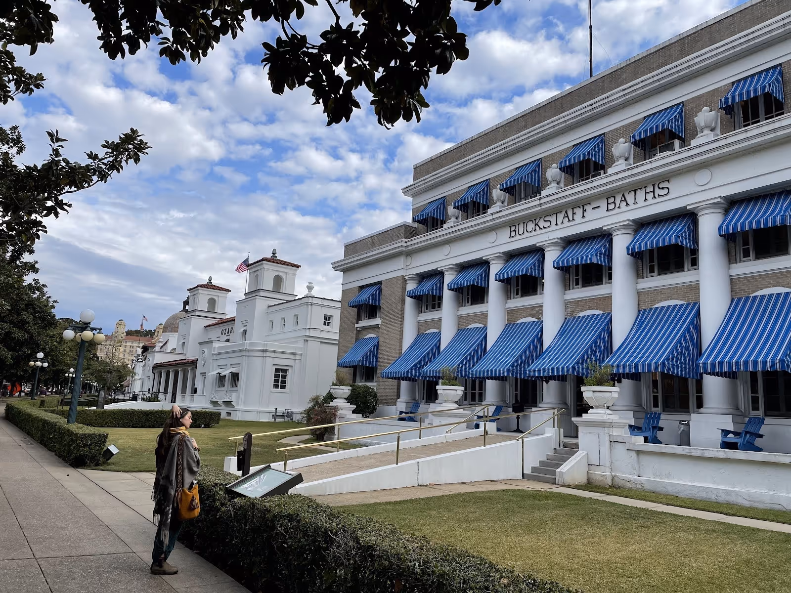 Street view of Buckstaff Bathhouse with blue striped awnings, a pedestrian on sidewalk, and neighboring white buildings in Hot Springs Arka.